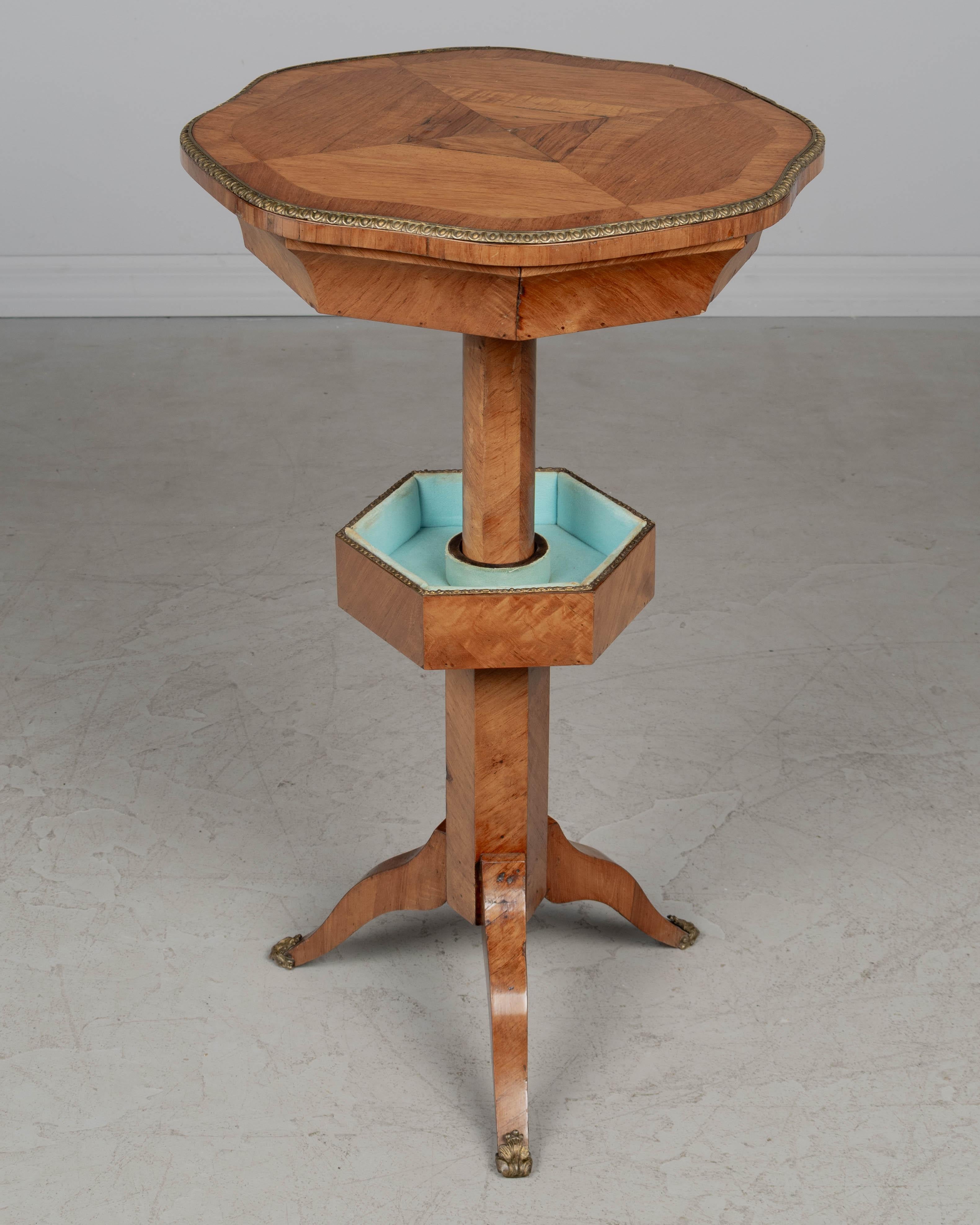 Table de couture à piédestal en marqueterie de bois fruitier Charles X du XIXe siècle, avec des compartiments étagés et tapissés de velours. Un fermoir en bois situé sous le grand compartiment octogonal caché permet de le maintenir en place. Plateau