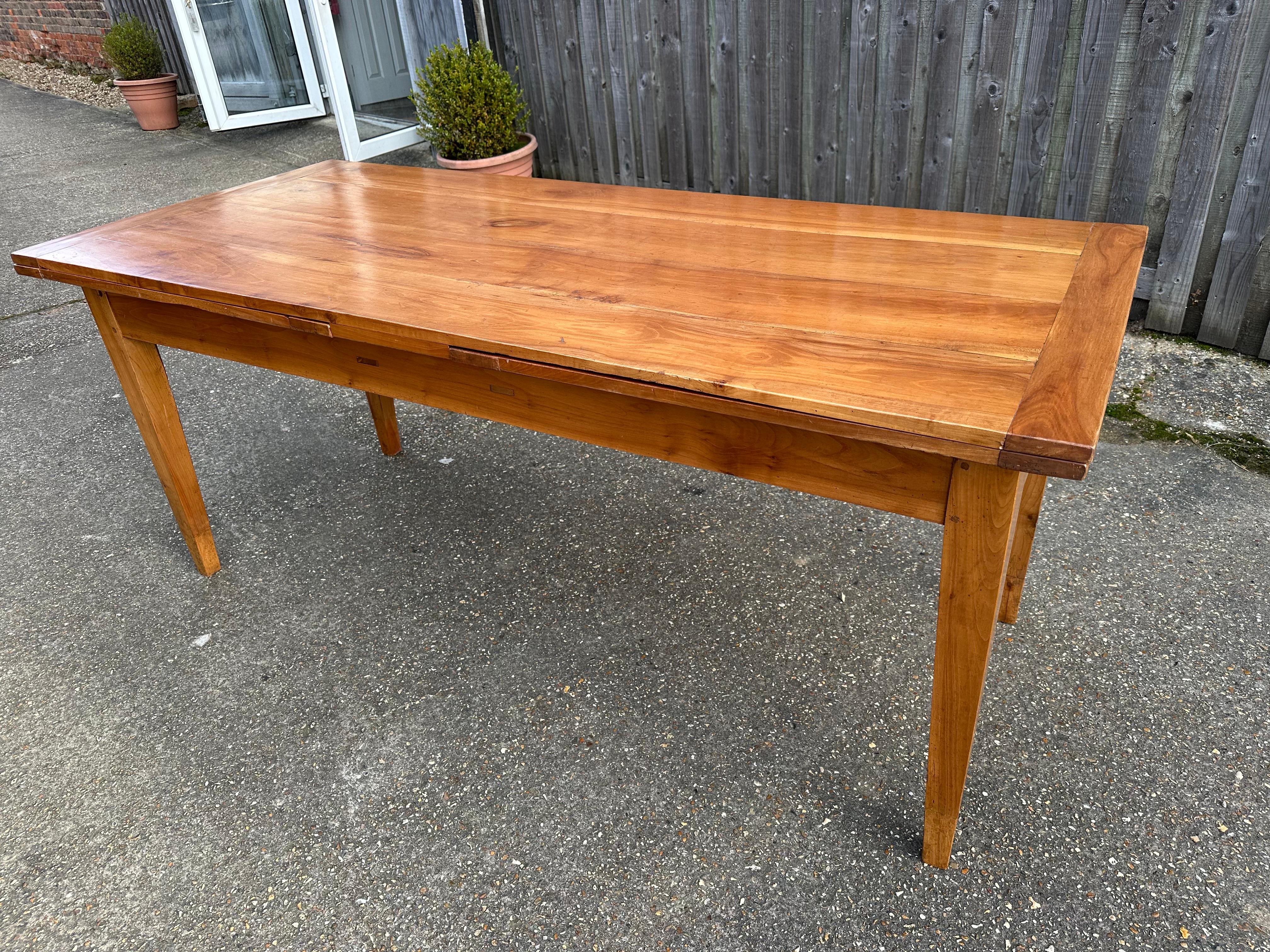 This 19th-century cherry double extending farmhouse table features a sturdy base with tapered legs and showcases a beautiful pattern and rich colour. It includes two extensions, each measuring 28.5 inches, allowing the table to reach a total length