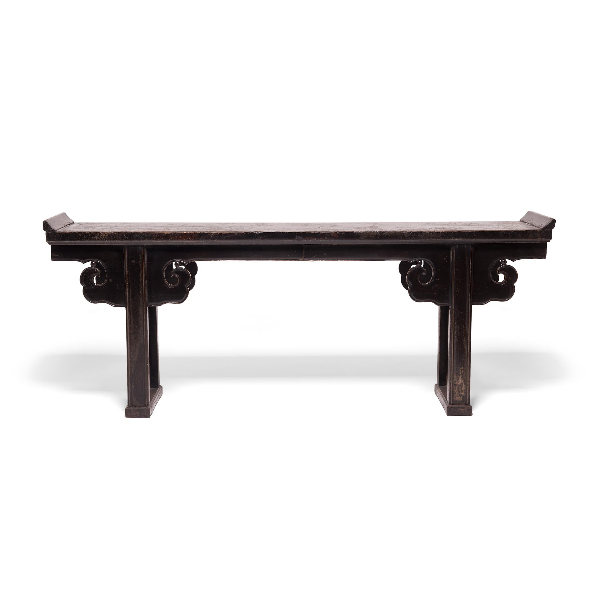 Created in China's Shanxi province in the early 19th century, this impressive altar table with everted ends features straight legs joined with a base stretcher, topped by hand carved spandrels resembling billowing clouds. Constructed with