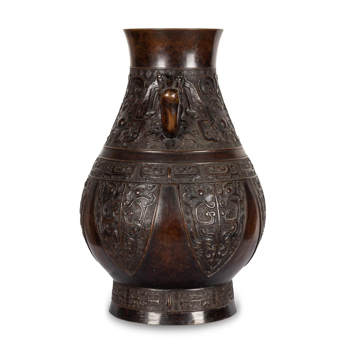 Vase chinois ancien du XIXe siècle en bronze, le corps en forme de poire reposant sur un pied étalé, le col cintré flanqué d'une paire d'anses en boucle provenant de têtes de dragon, coulé en bas-relief à l'extérieur avec deux larges bandes