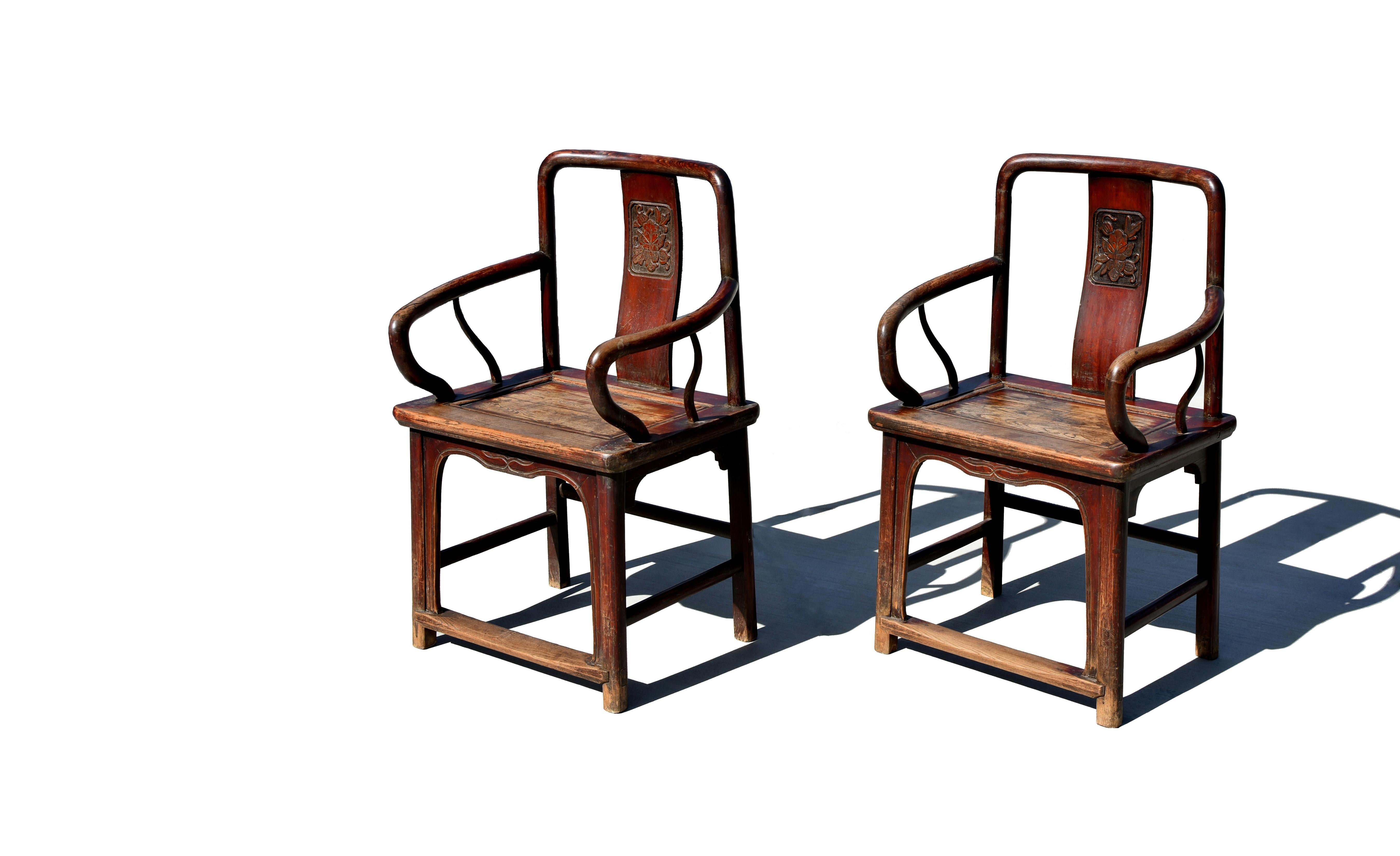 A pair of large 19th century Chinese elmwood armchairs. An elegant crestrail meets the back stiles which extend all the way through the member of the seat frame to become the back legs. The solid splat carved with a peony descends from the center of