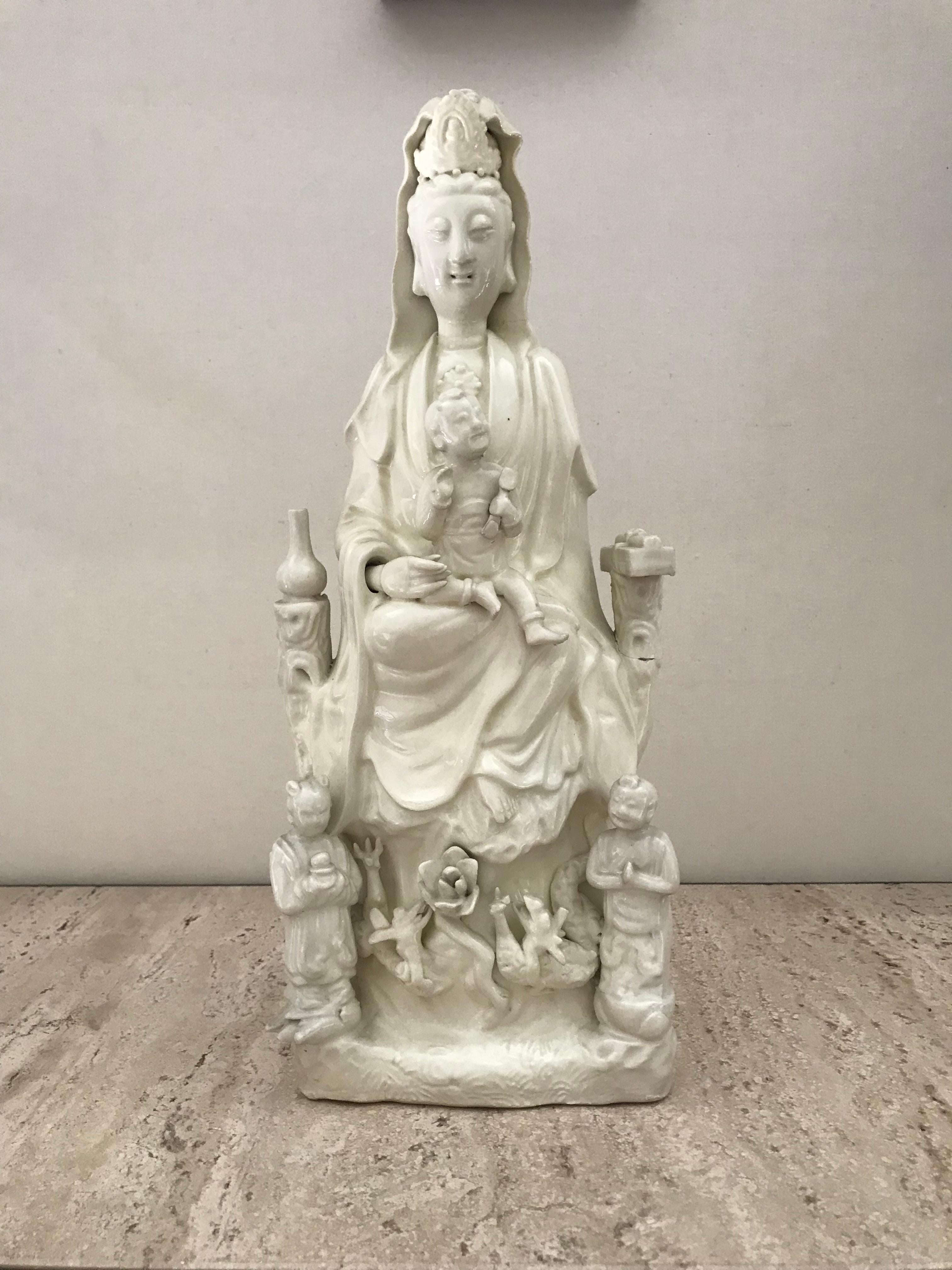 Chinise blanc-de-chine figure of Guanyin

The goodness seated on a rockwork base applied with a pair of dragons and a lotus head, with a young boy on her knee, flanked by two acolytes, a book and a pear shaped vase.
Some damages and old repairs.