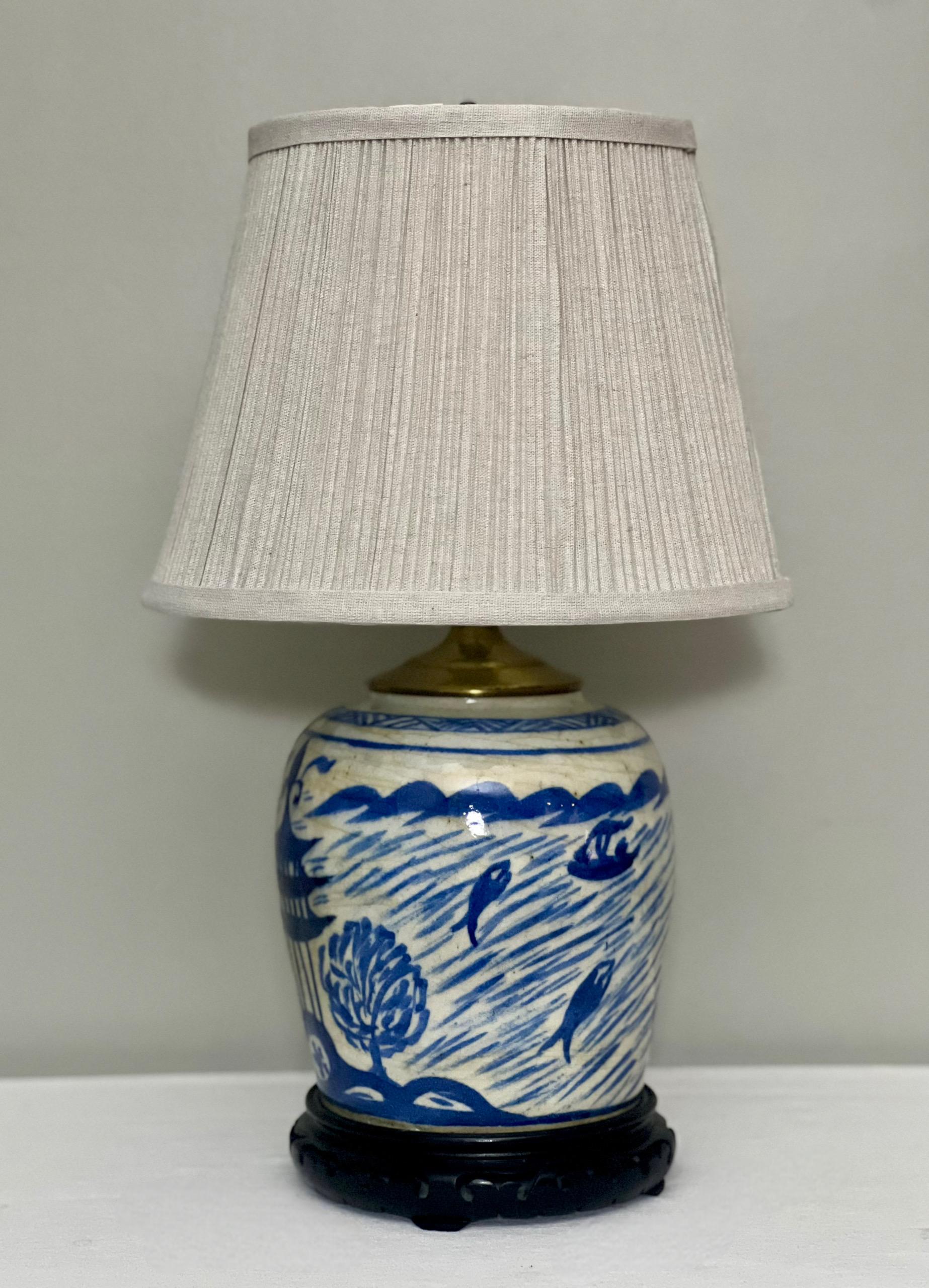 Antique Chinese blue and white ginger jar converted to a lamp with brass fittings set on an ebonized hardwood base, late 19th century. It depicts a hand-painted tranquil river scene with fishermen in boats, fish and architecture. Beautiful piece for