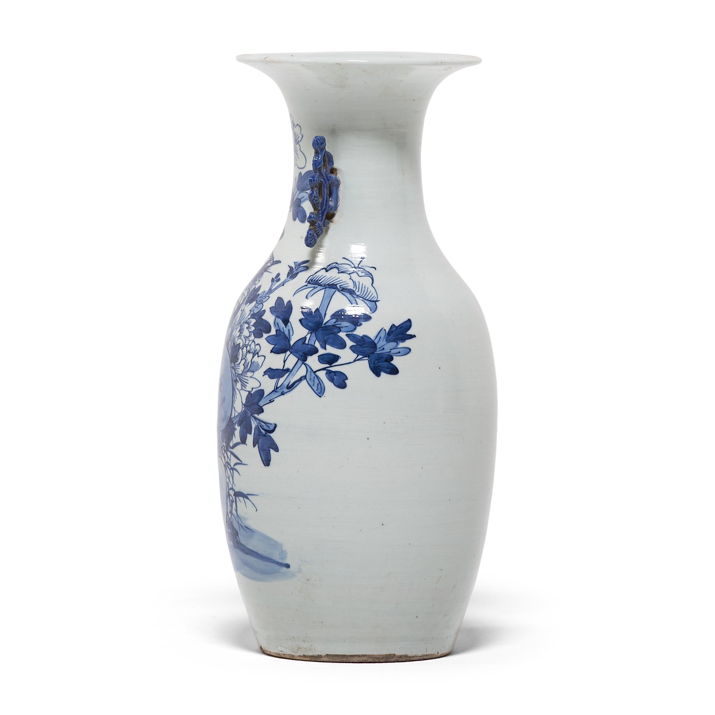 This exquisite 19th century porcelain vase has a gently tapered body and a dramatic flared lip, flanked by two molded scroll handles. Painted with expressive brushwork, the vase is festooned with peony blossoms, emblems of spring time and feminine