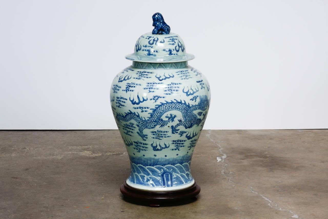 Monumental 19th century Chinese blue and white porcelain ginger jar or temple jar. Features a dragon amid clouds with crashing waves below. Topped with a foo dog on the the lid and resting on a carved wooden stand with shaped feet. Beautifully