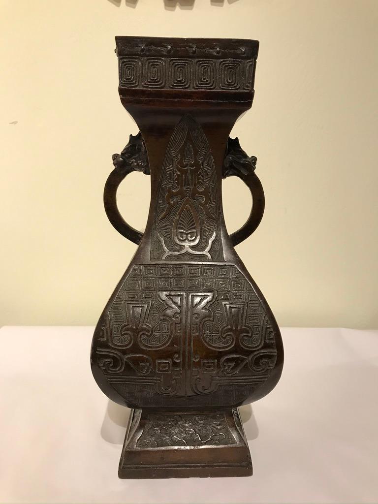 A handsome Chinese bronze two handled vessel with geometric top and base. The body decorated with etched Archaistic designs, the handles with dragon head terminals. This piece has a wonderful deep mocha patina. Stamped mark on base.