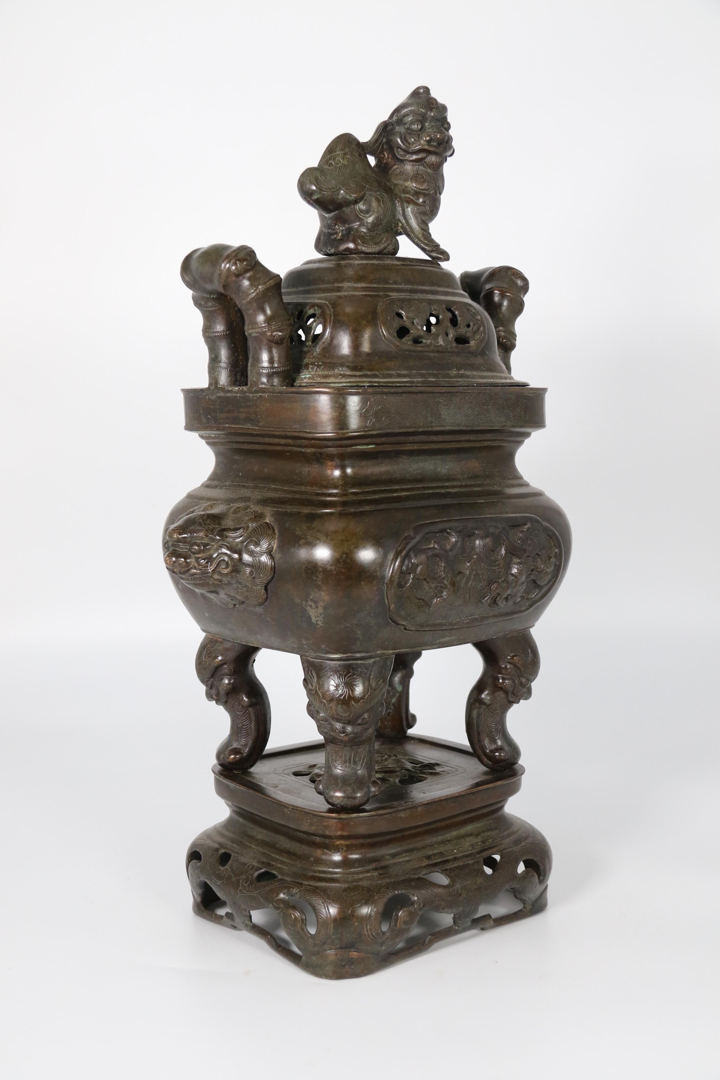 This large Chinese bronze censer dates to circa 1860. It is made in three parts, stand, vessel, and lid. The lid has pierced decorative panels with pine trees and a bold Buddhist lion finial for lifting.
The censer has lifting handles in the shape
