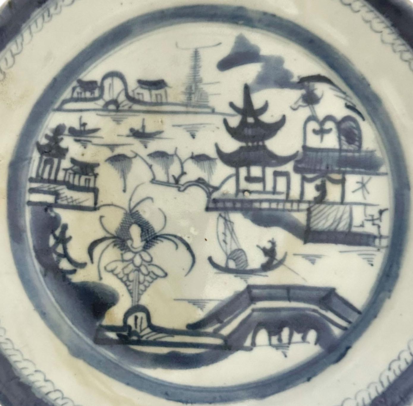 Assiette classique en porcelaine bleue et blanche de Canton, peinte à la main au XIXe siècle, représentant une scène de village tranquille au bord d'une rivière, avec une architecture traditionnelle, des arbres et des bateaux. Les tons doux de