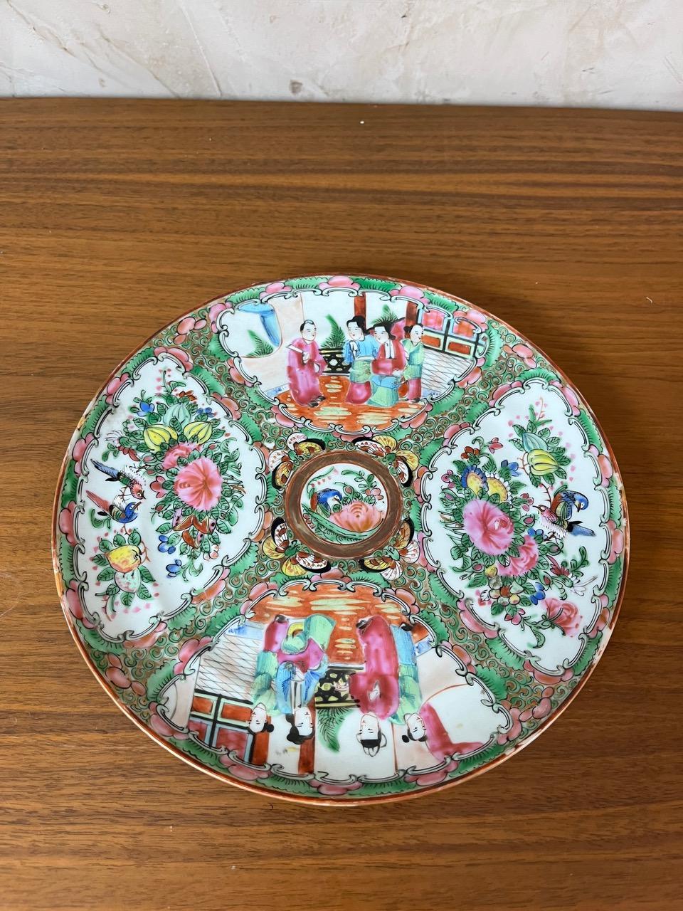 Beautiful decorative plate in Chinese porcelain, Rose Canton style, dating from the 19th century. It is richly adorned with traditional Chinese scenes, flowers, exotic birds, and figures in traditional attire. The vibrant colors and meticulous