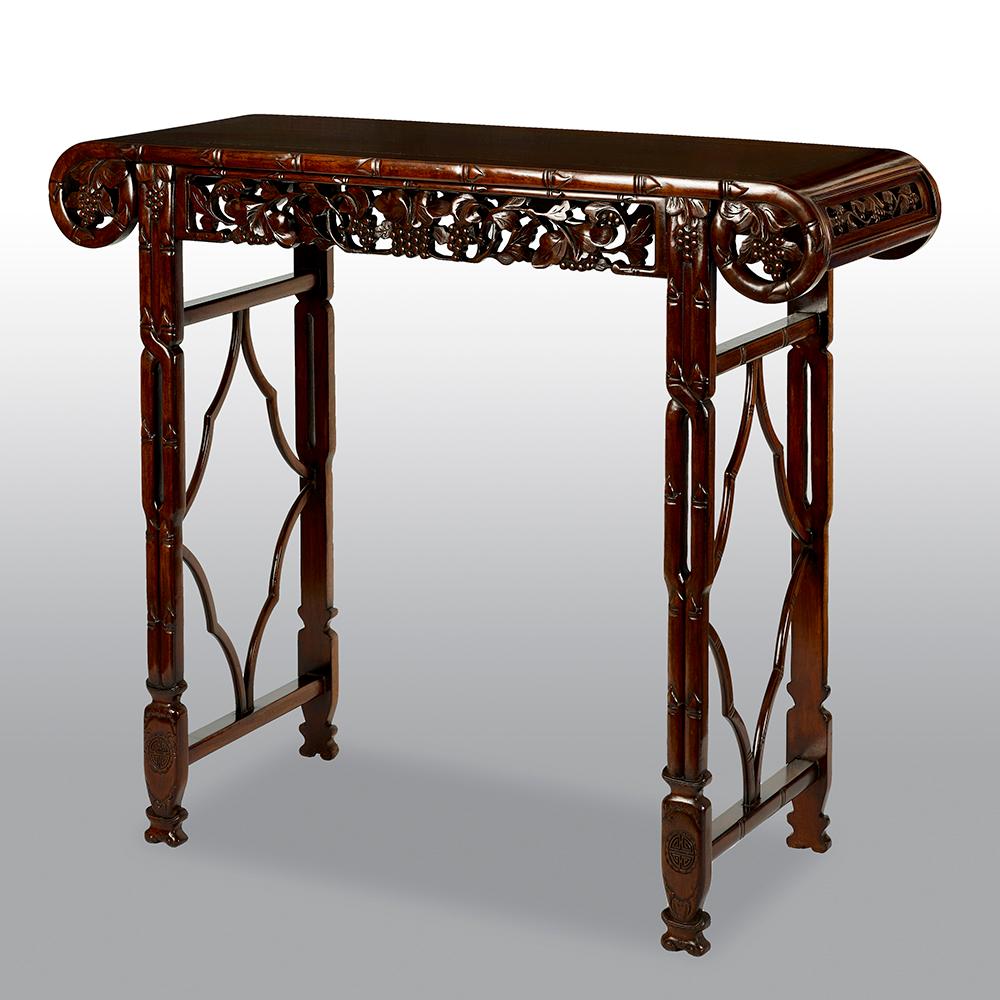 A 19th century Chinese hardwood carved alter table having a panel top, carved scrolling ends. The frieze with carved fruit and leaves, end support each with stretchers and terminating in scrolling carved feet.