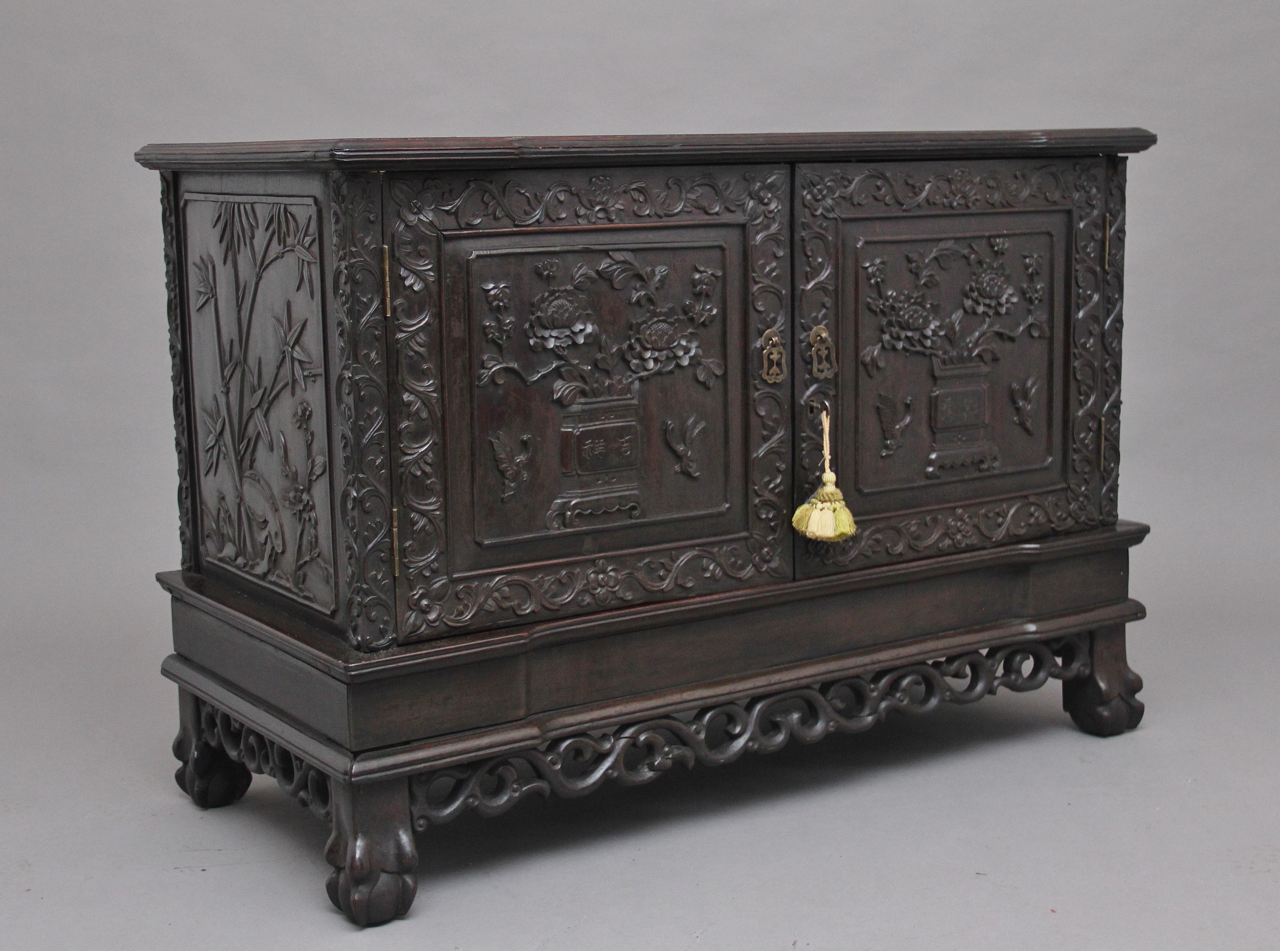 19th century Chinese hongmu hardwood carved cabinet, the shaped and moulded top above two cupboard doors opening to reveal a single fixed shelf inside, the door fronts profusely carved all-over with emerging foliage and vines, as with the sides of