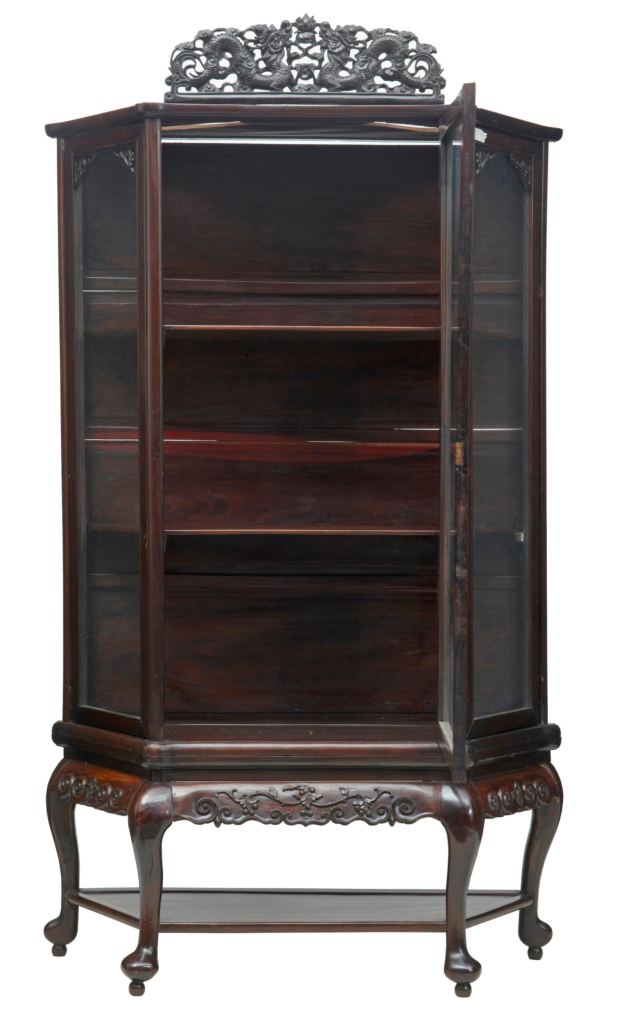 19th century Chinese carved hardwood glazed display cabinet, circa 1890

Single large glazed door opens to 2 shelves, stands on 4 shaped legs united by a shelf. Detachable pierced carving of dragons to the top, this would have been flanked either