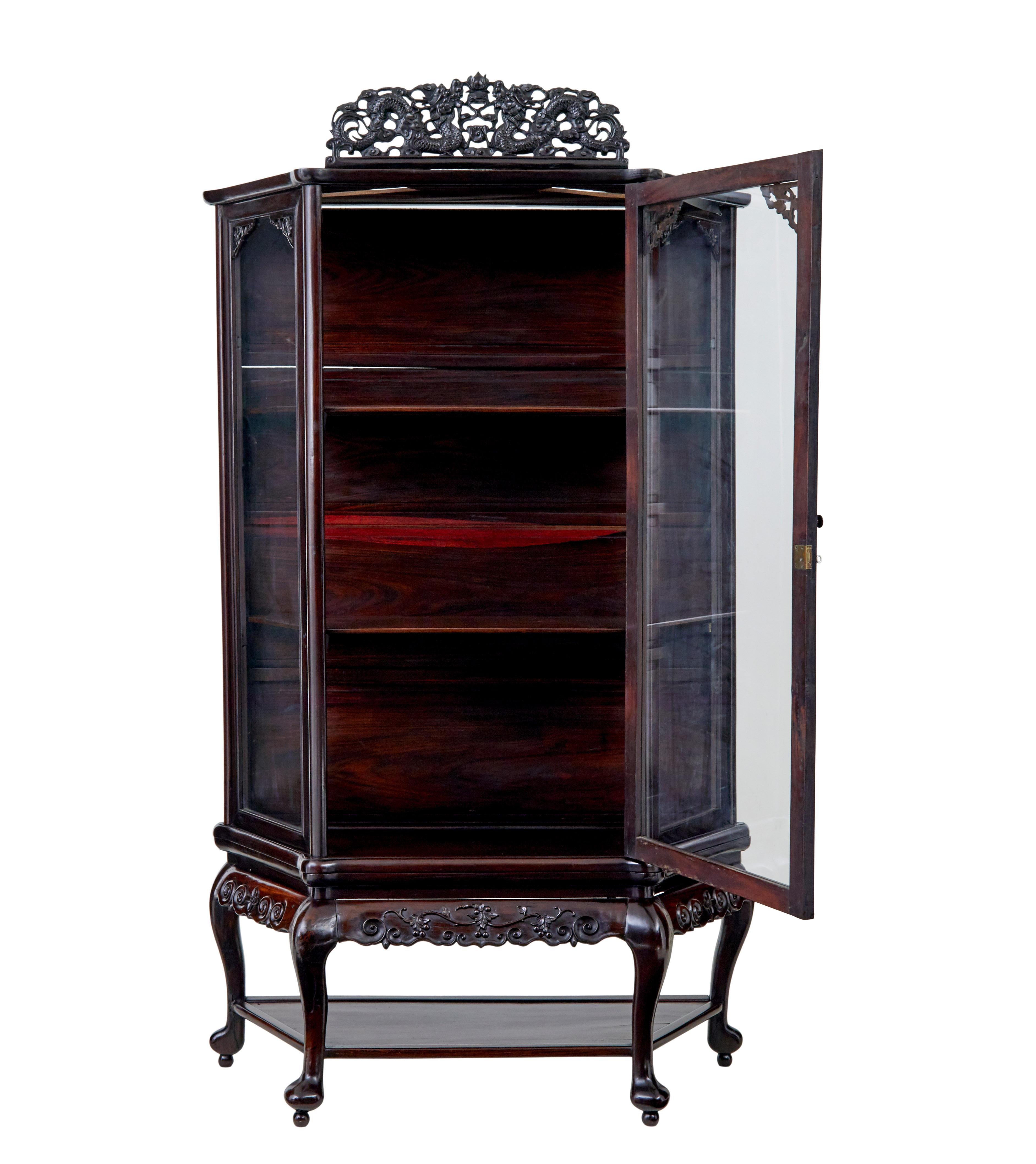 19th century Chinese carved hardwood glazed display cabinet circa 1890

Single large glazed door opens to 2 shelves, stands on 4 shaped legs united by a shelf. Detachable pierced carving of dragons to the top, this would have been flanked either