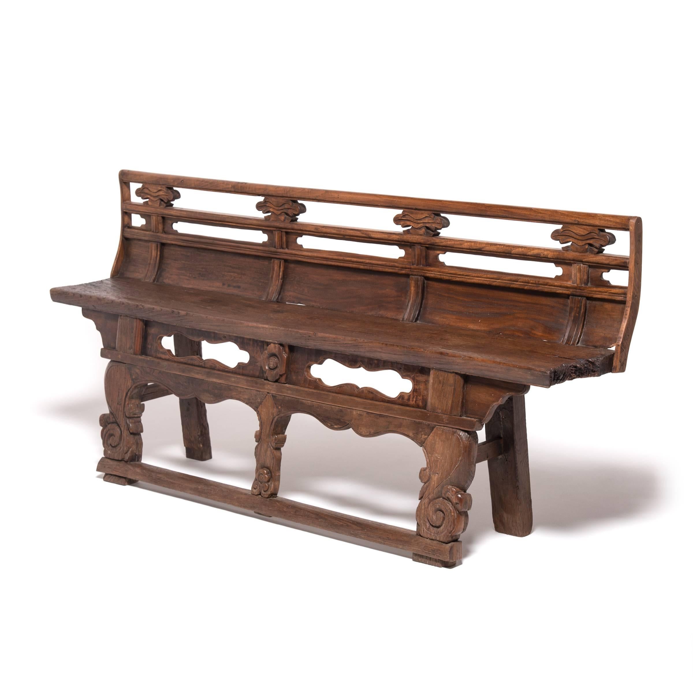 This 19th century village bench from China's Shanxi province is an exceptional example of Qing-dynasty craftsmanship. Unusual for its high back, built-in footrest, and ornate carved decorations, this bench was likely made for an opera house,