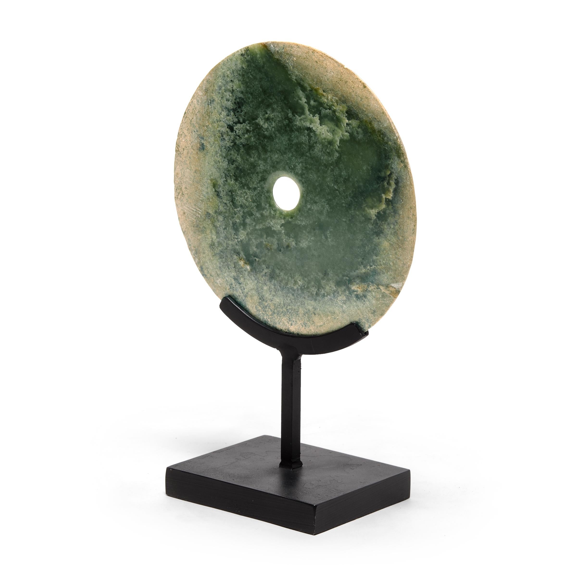 Subtly contrasting jade occlusions give this round bi disc a certain celestial quality, like a full moon obscured by darkened clouds. Found in the tombs of ancient Chinese emperors and aristocrats, bi discs such as this have a mysterious and