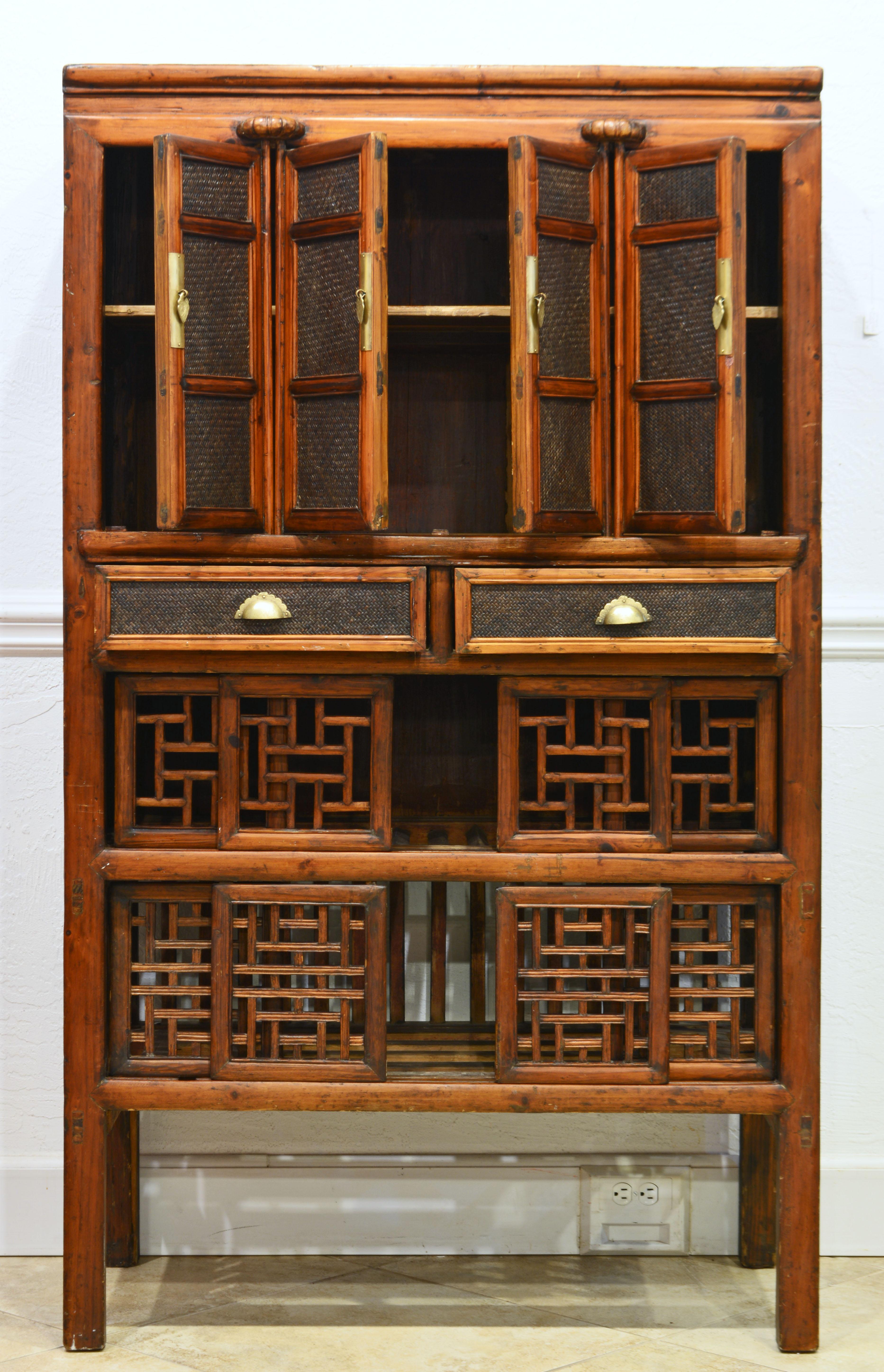 This Chinese cabinet of functional and beautiful design dates to the late 19th century. It features four cane paneled doors opening up to a shelved interior above two cane front drawers. The lower part has ornamental Chinese open work sliding doors