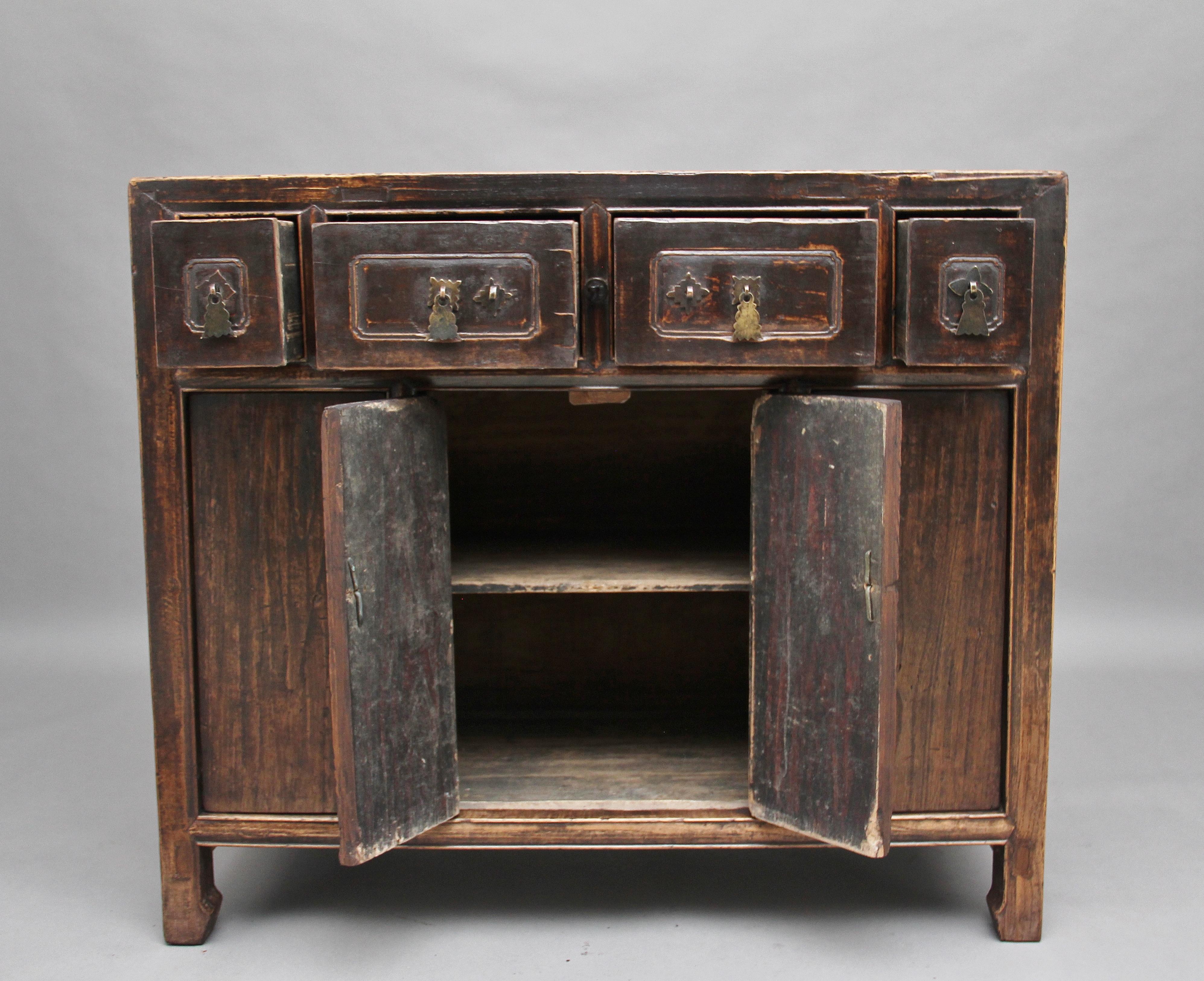 19th century Chinese elm dresser / cabinet, having a selection of four drawers at the top with carved decoration on the drawer fronts, original brass handles, four door cupboard below opening to reveal a fixed single shelf inside, standing on scroll