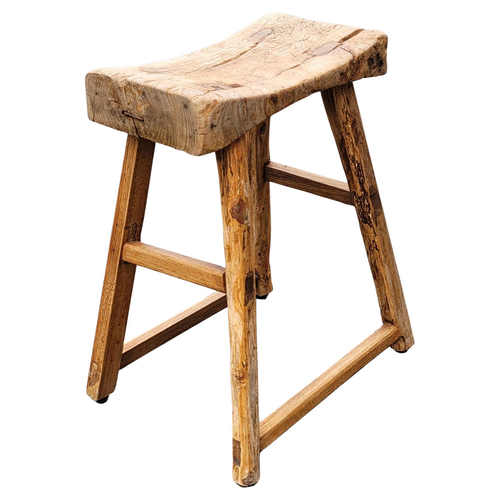 Dated to mid 19th century, this rustic, farmhouse, primitive and brutalist stool has simple splayed-leg design and well-worn finish. Crafted of northern elm wood with mortise-and-tenon joinery, without the use of nails or screws, the stools feature
