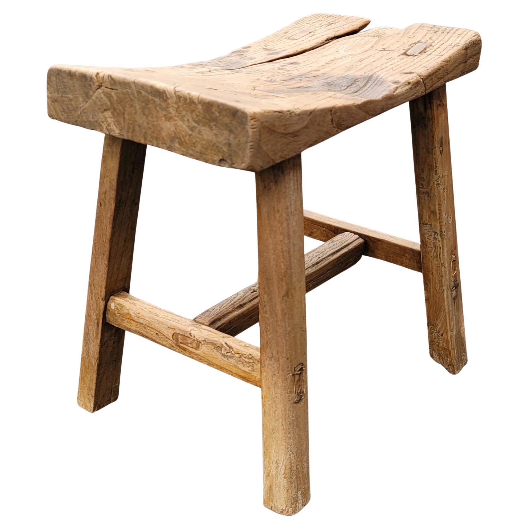 Dated to mid-19th century, this rustic, farmhouse, primitive and brutalist stool has simple splayed-leg design and well-worn finish. Crafted of northern elm wood with mortise-and-tenon joinery, without the use of nails or screws, the stools feature