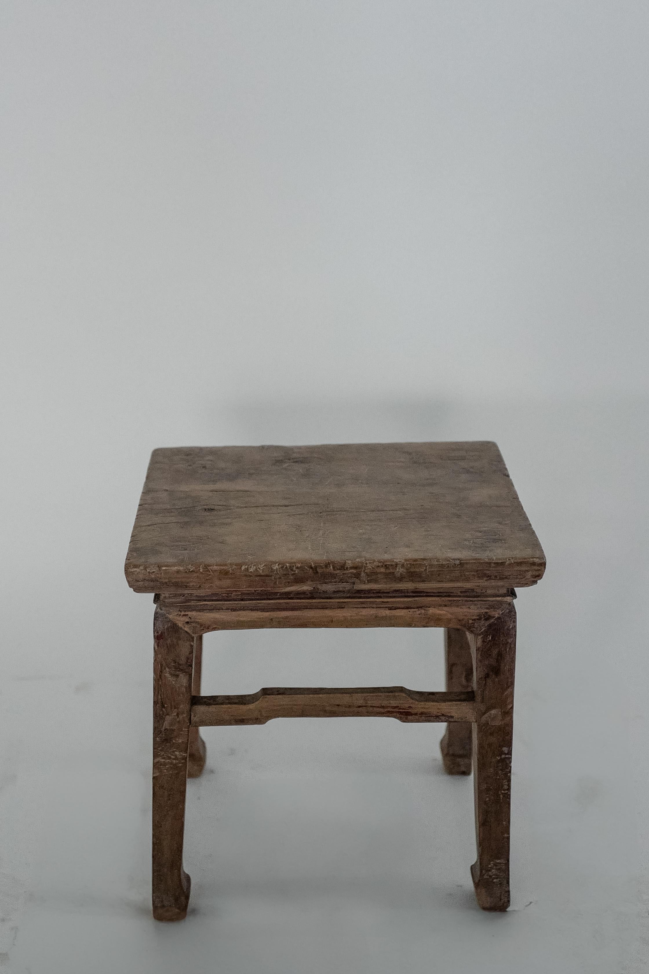 This charming 19th-century Chinese side table crafted from elm wood exudes rustic elegance. With its simple, minimalist design this antique piece reflects the timeless beauty of Qing dynasty furniture. Its naturally aged patina and distressed finish