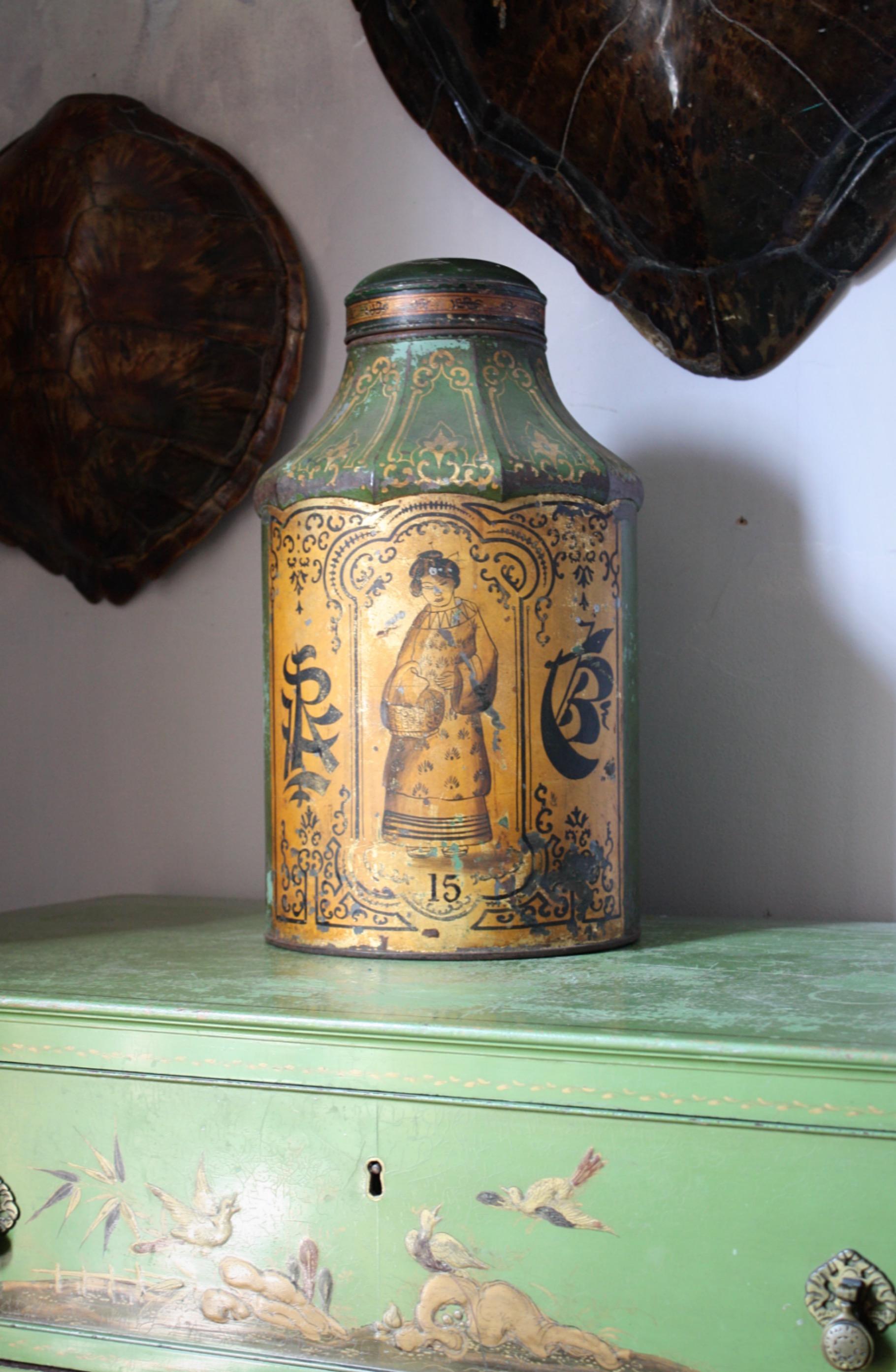 A highly decorative green ground and gilt decorated sheet metal (toleware) tea canister.

Of cylindrical form with incurved top, elaborately decorated with a central cartouche enclosing a Mandarin figure set above the number 15, flanked by Chinese
