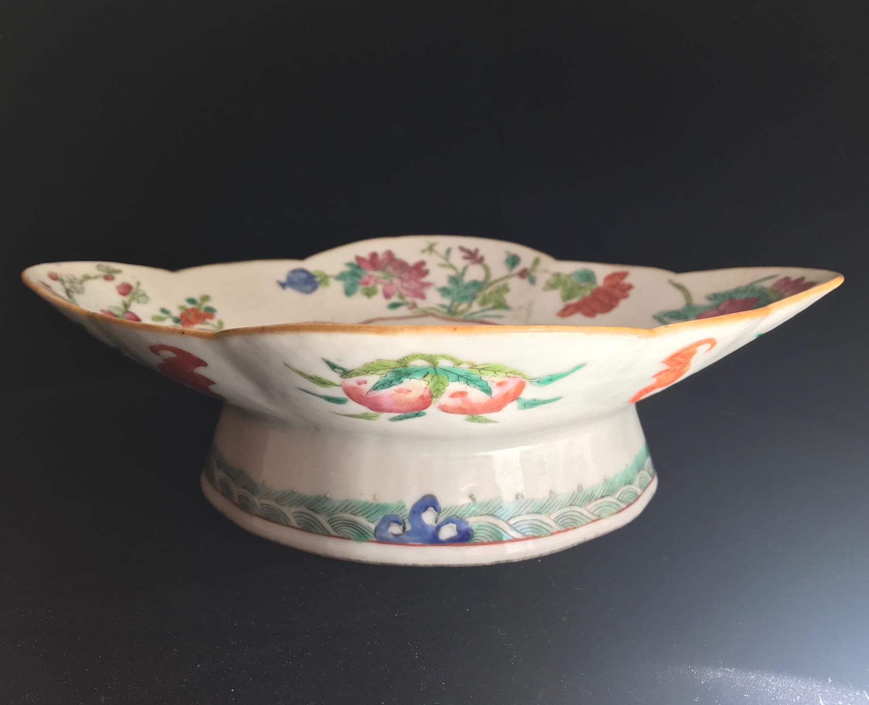 The footed bowl is hand painted in enamel, showing an Immortal resting on a large root. The figure is accompanied by an inscription identifying the character. The exterior is decorated with various fruits and flying bats, an auspicious symbol of
