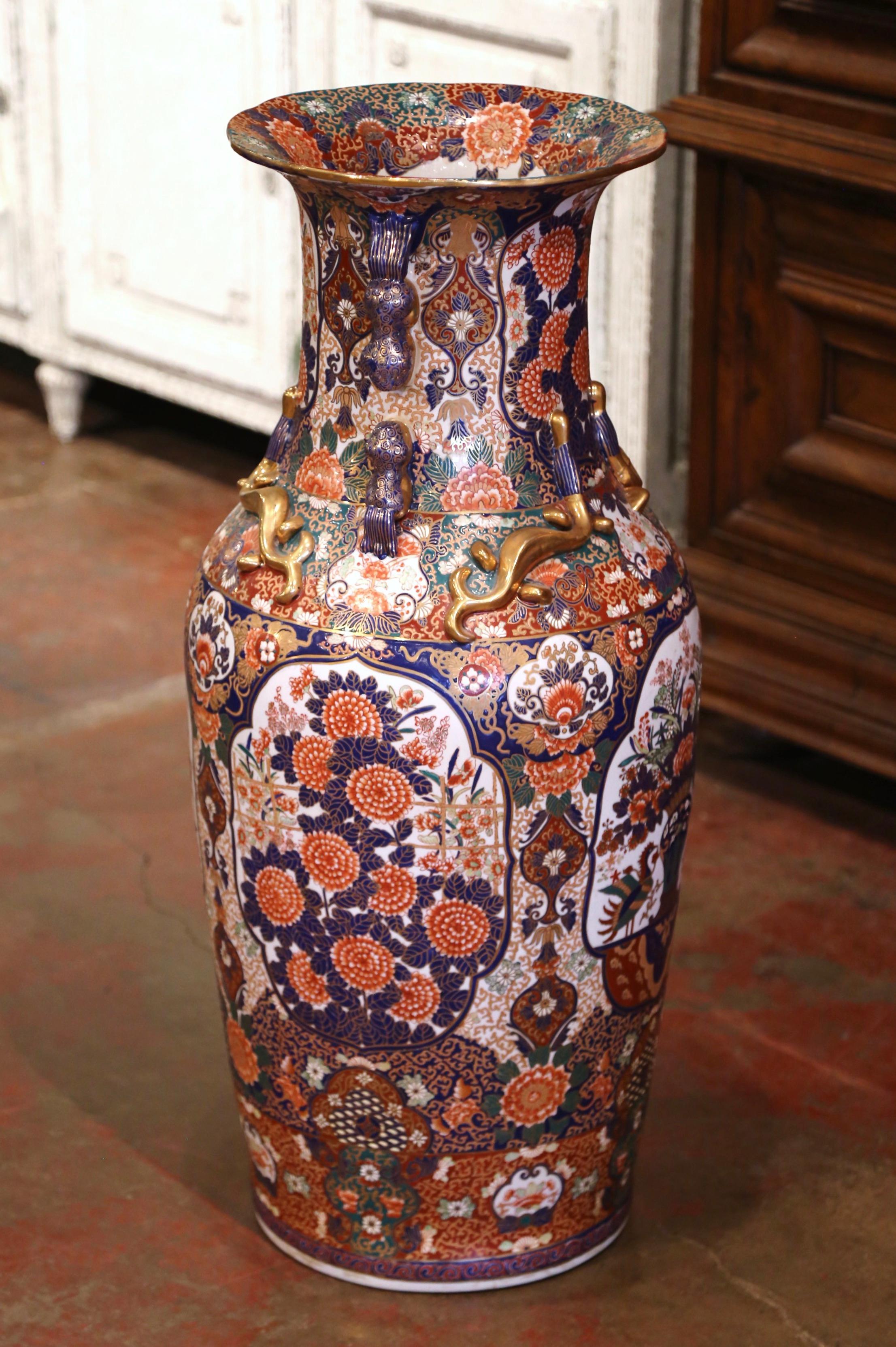 Crafted in China circa 1920, the tall Family Rose vase is round in shaped with an elegant long neck decorated with gilt Foo Dogs and dragon lizards in high relief. The colorful antique urn features hand painted flower vases medallions and floral