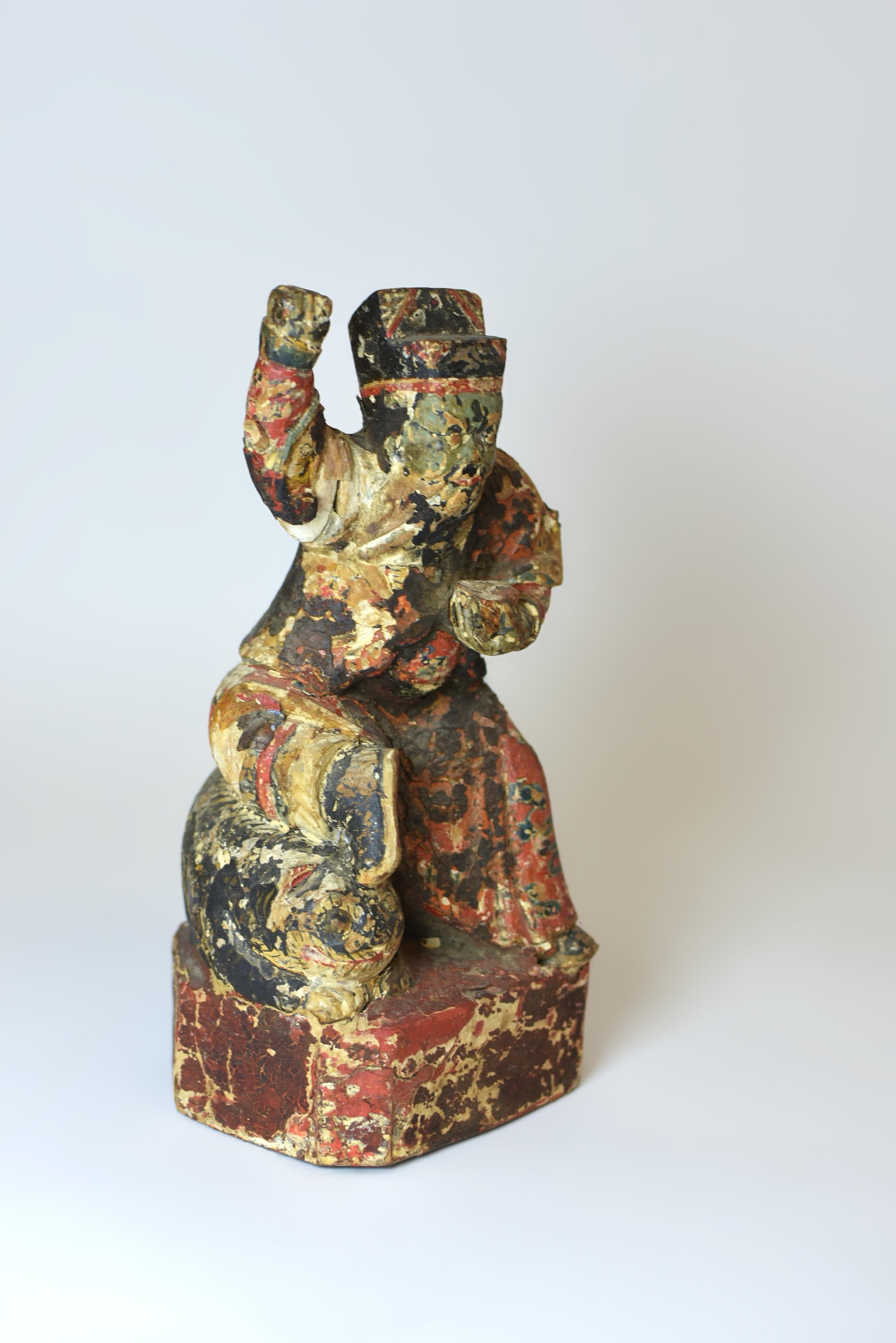 This 19th-century hand-carved polychromatic wood figure depicts a powerful Guardian, poised on a recumbent tiger with his right fist raised in a striking motion, his eyes bulging with fierce determination. In his left hand, he wields a scepter to