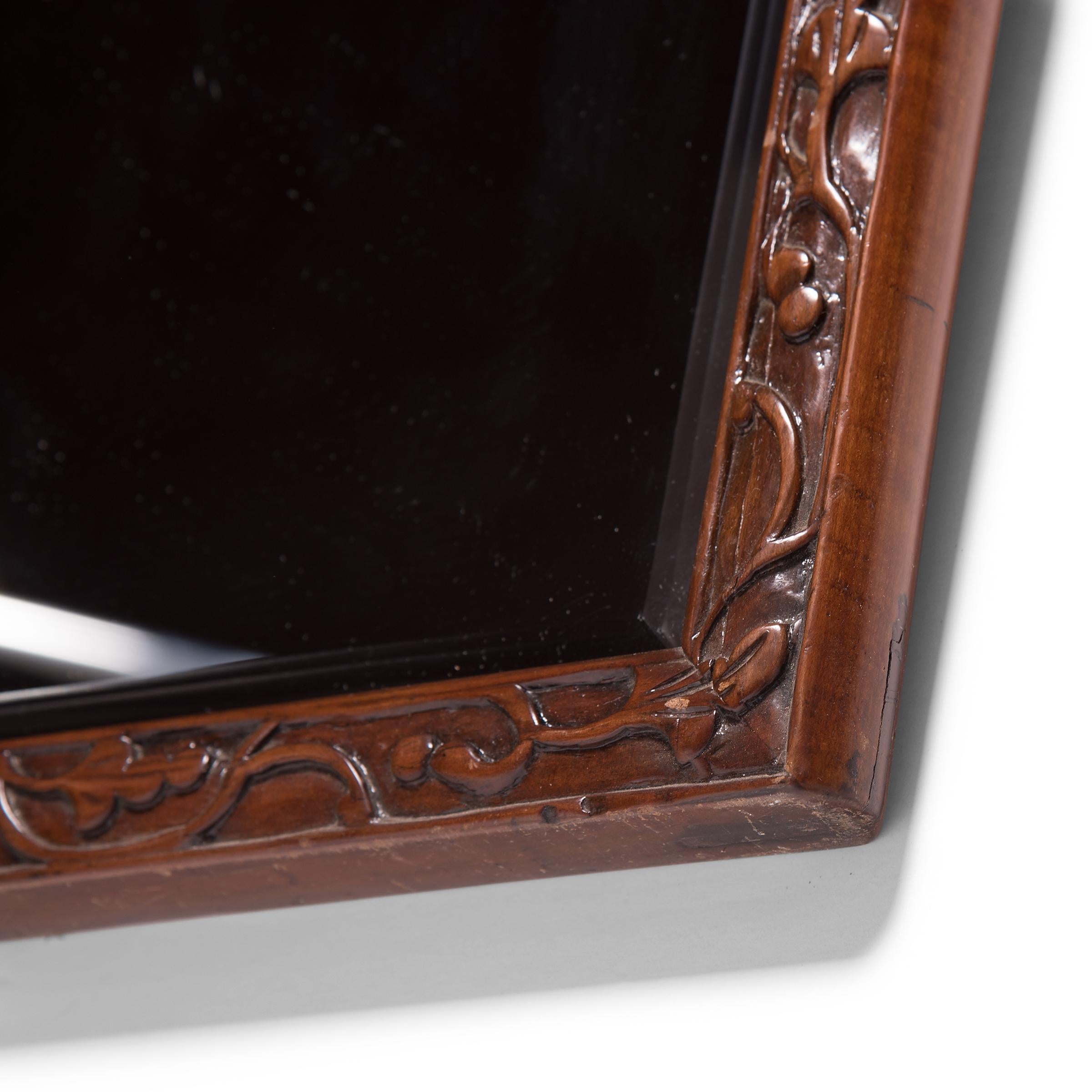 This contemporary bevelled mirror is set in an antique walnut frame hand carved with a flowered trailing vine motif. Chosen for its rich color and open grain, walnut was the ideal wood for realizing the high level of workmanship characteristic of