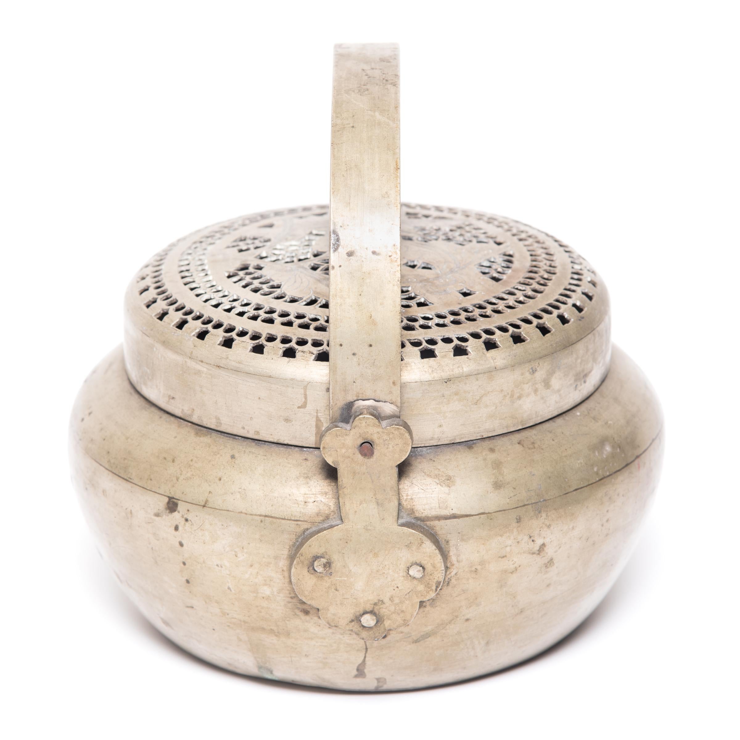 This 19th century handcrafted bronze hand warmer would have been owned by a woman of means and filled with coals so she could warm her hands on cold winter nights. The top is beautifully pierced with a flowering bud design. Surrounding the flowers