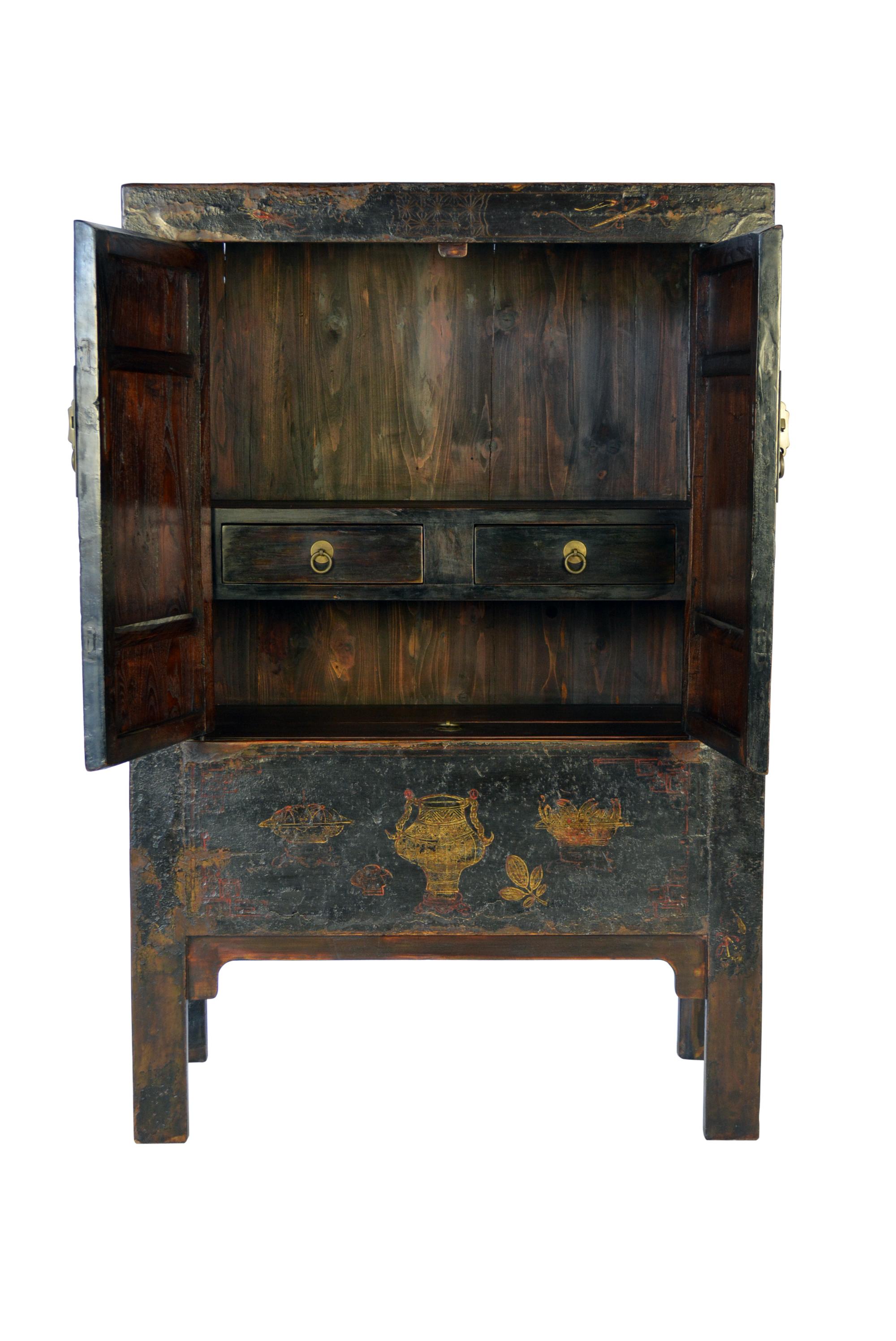 This 19th century Chinese linden wood cabinet stands square and proud with a rich, well-preserved black lacquer finish and traces of its original gilt decoration. From the remaining traces of its paintings, we can see motifs of the eight treasures