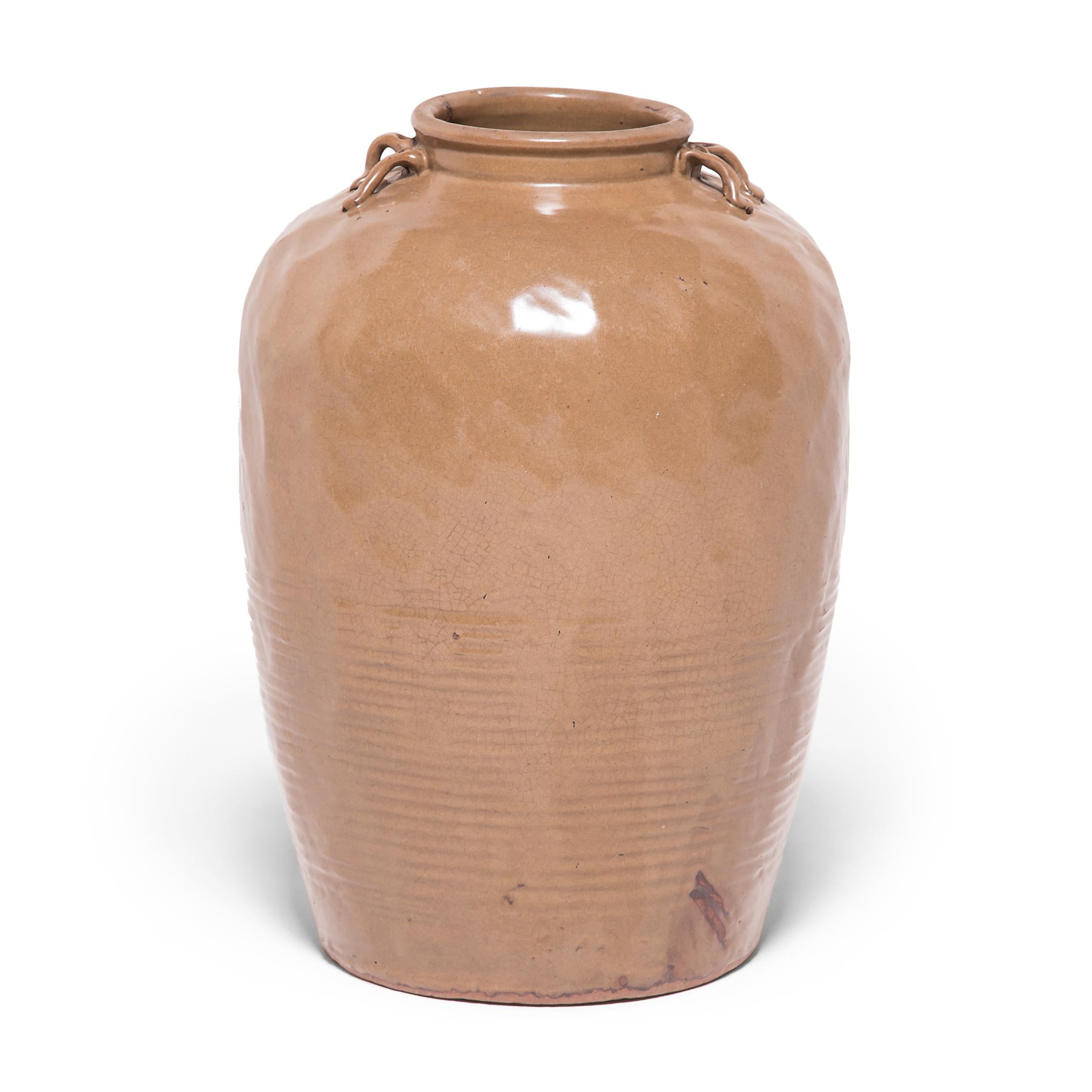 In 19th century China jars like this would have held wines, foods, and other consumable items. The combination of an irregular surface with a subtle ridged pattern along the side gives this tall vessel an understated sculptural presence. Spots of