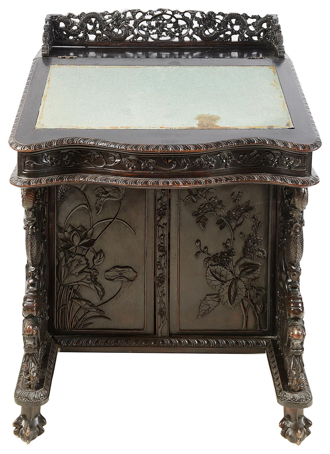 A rare 19th century Chinese hardwood Davenport, having wonderful carved mythical dragons, scrolling grapevine and floral decoration. The writing slope opens to reveal compartments within, four drawers to the side and raised on claw feet.