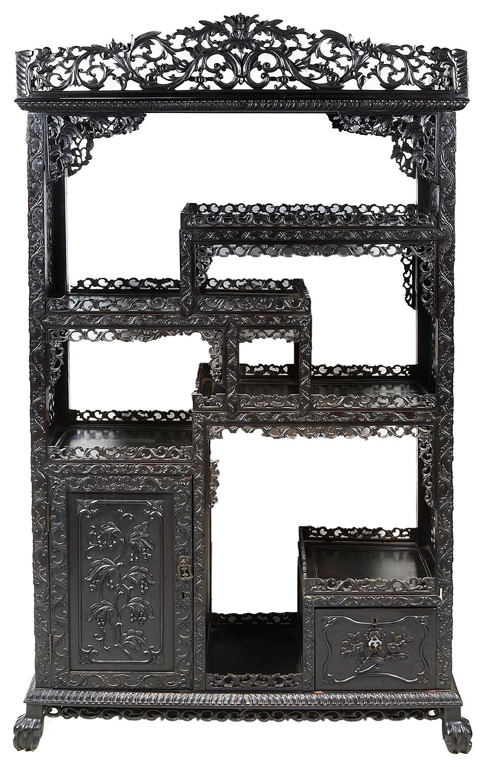 A good quality set of 19th century Chinese hardwood floor standing shelves, having wonderful hand carved decoration depicting scrolling foliage, berries and flowers, carved fretwork panels to the sides, paneled doors beneath and raised on carved