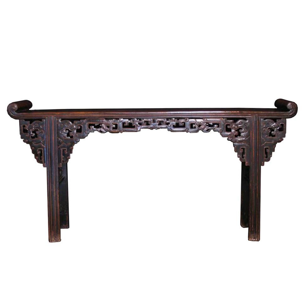 Chinese Provincial-style Altar table, a large semi-hardwood table with upturned scroll end pieces, the solid plank top of a checked and feather grained wood, the front pierced skirts with raised scrolling vine or key fret pattern having dragon heads