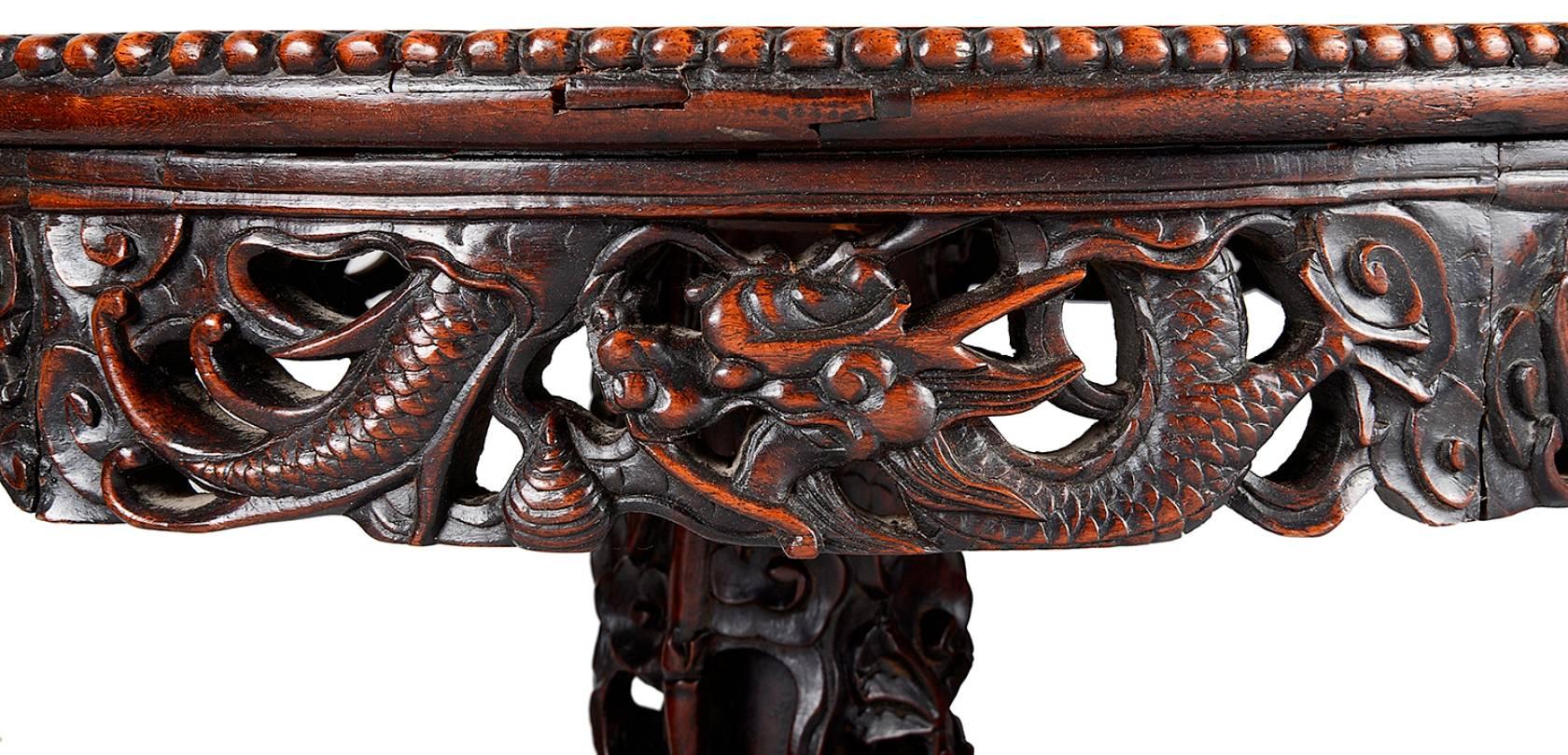 A good quality 19th century Chinese hardwood side table, having an inset panelled top with carved foliate decoration, the frieze with hand carved mythical dragons entwined. Raised on a carved central pedestal also with wonderfully carved dragons and