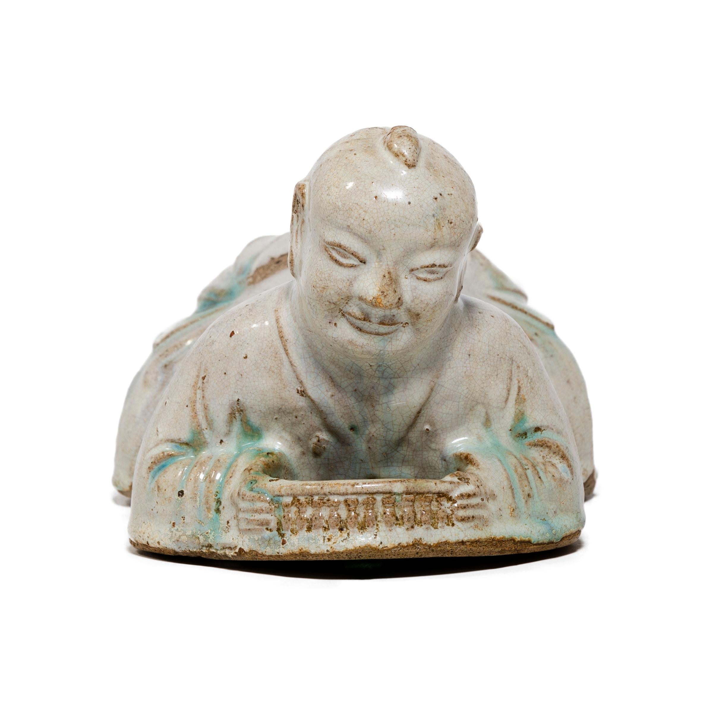 To keep her elaborate hairstyle intact while sleeping, a well-to-do Qing-dynasty woman once used this ceramic headrest as a pillow. This headrest is shaped in the form of a “Ho Ho” boy and would have been used to invoke good fortune. Children were a