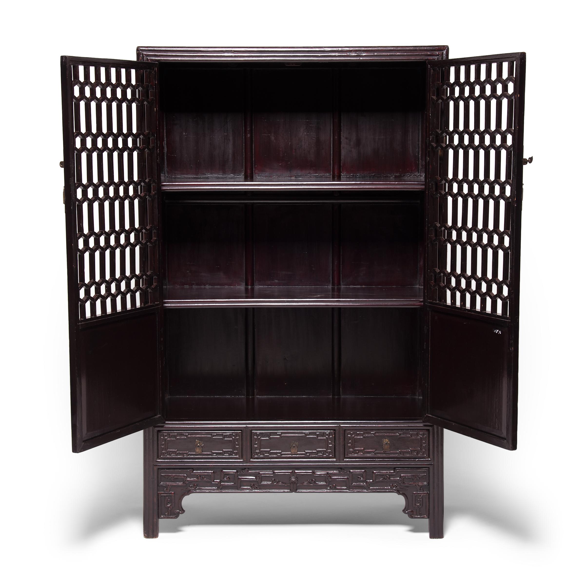 This beautiful early 19th century display cabinet from China's Henan province features complex honeycomb lattice panels and doors carved with elaborate scrollwork. Unlike fretwork made by carving or perforating a solid panel, this lattice would have