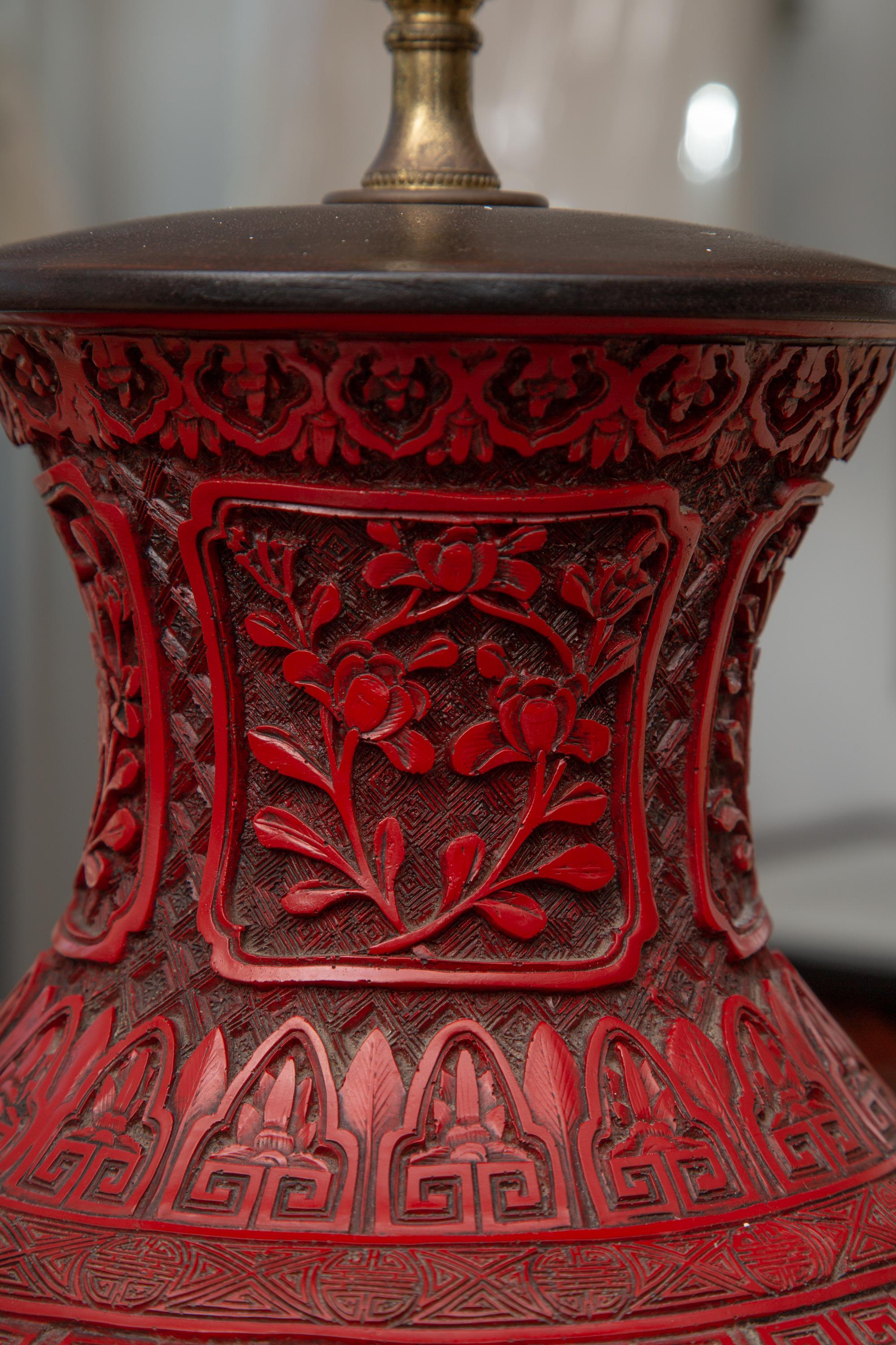 This is a stunning Chinese cinnabar vase is intricately carved with Chinese figures and natural elements, situated on a rosewood base. 19th century.