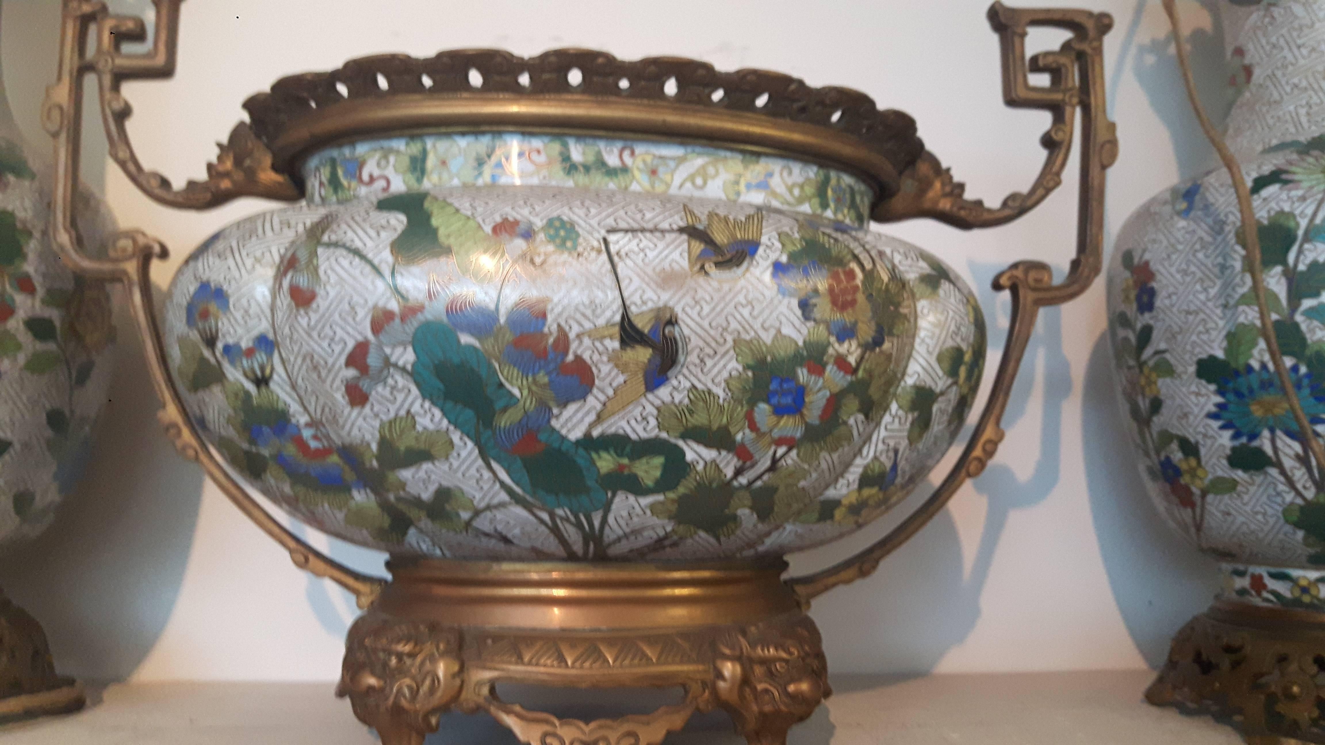 Raffinata guarnitura francese a tre pezzi in smalto cloisonne montata su ormolu con decorazione applicata di farfalle, fiori e rami. I vasi vengono trasformati in lampade.