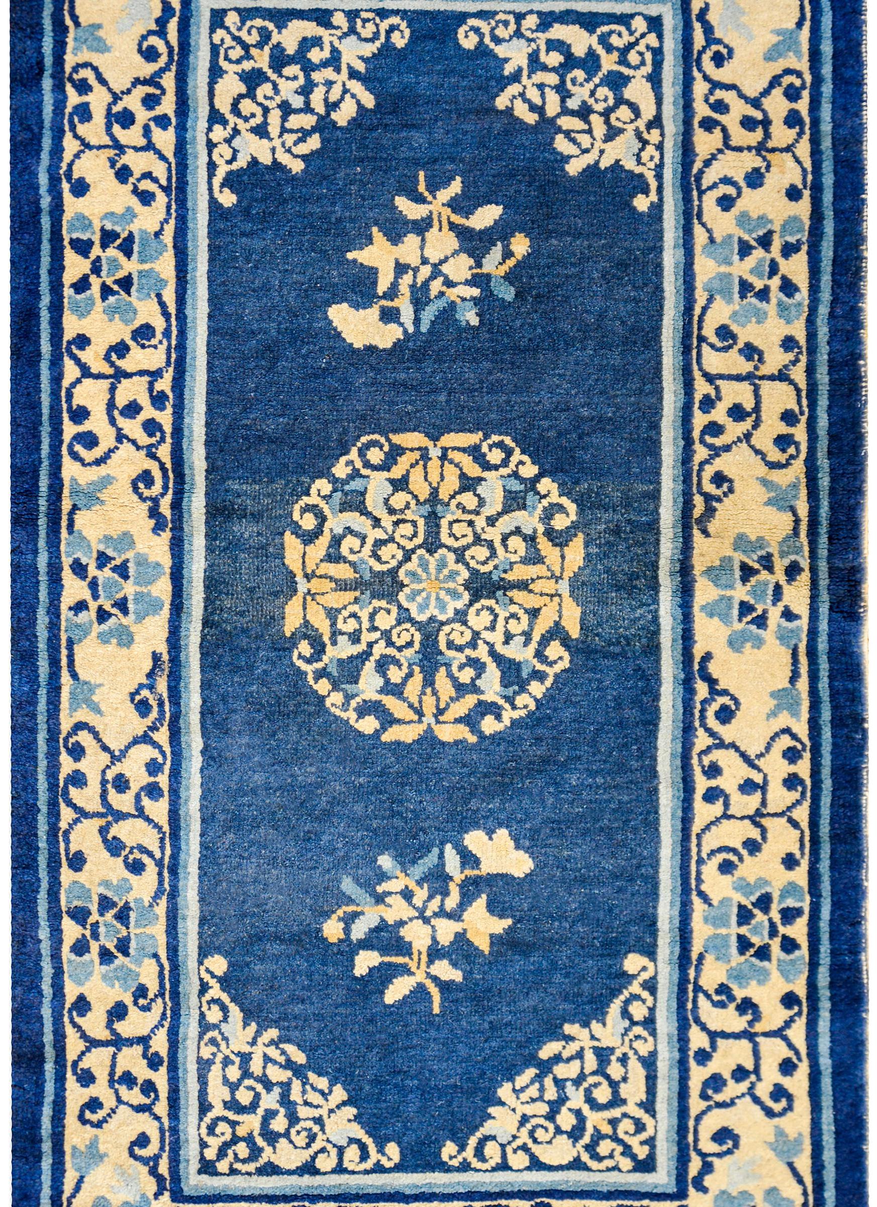 A late 19th century Chinese Peking rug with one large central floral medallion with four lotus blossoms woven in cream, gold, and light indigo, on a dark indigo field of flowers. The border is really well rendered with a stylized peony and scrolling