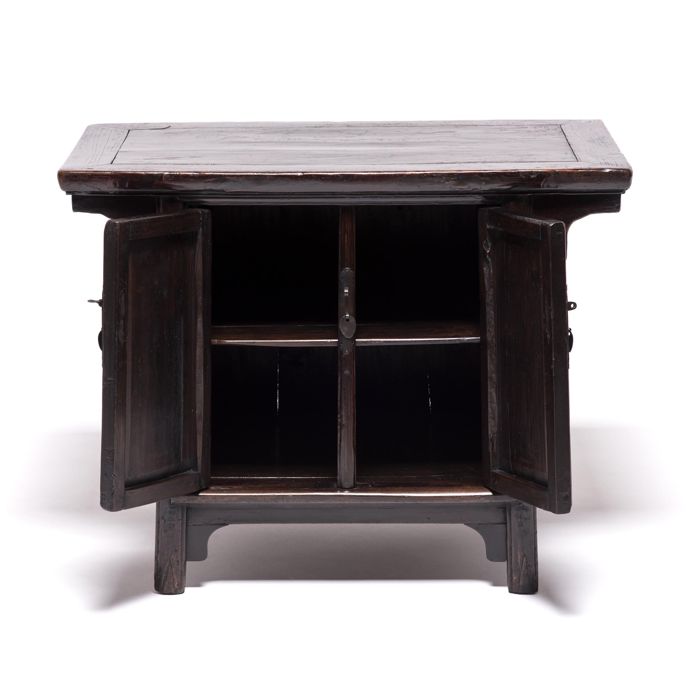 Perfectly proportioned for its petite size, this elmwood chest supports a table top with curving spandrels - echoed in the gentle curves of its apron base and rounded feet. A handcrafted brass fixture with a triple-dagger post adds to the chest’s