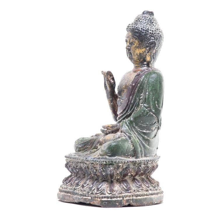 Figure of Buddha depicted seated in dhyanasana on a double lotus base with his left hand in dhyanasanamudra and the right hand raised. Wearing a draped sanghati with his hair in tight knots surmounted by an ushinisha. There are traces of gilt, red,
