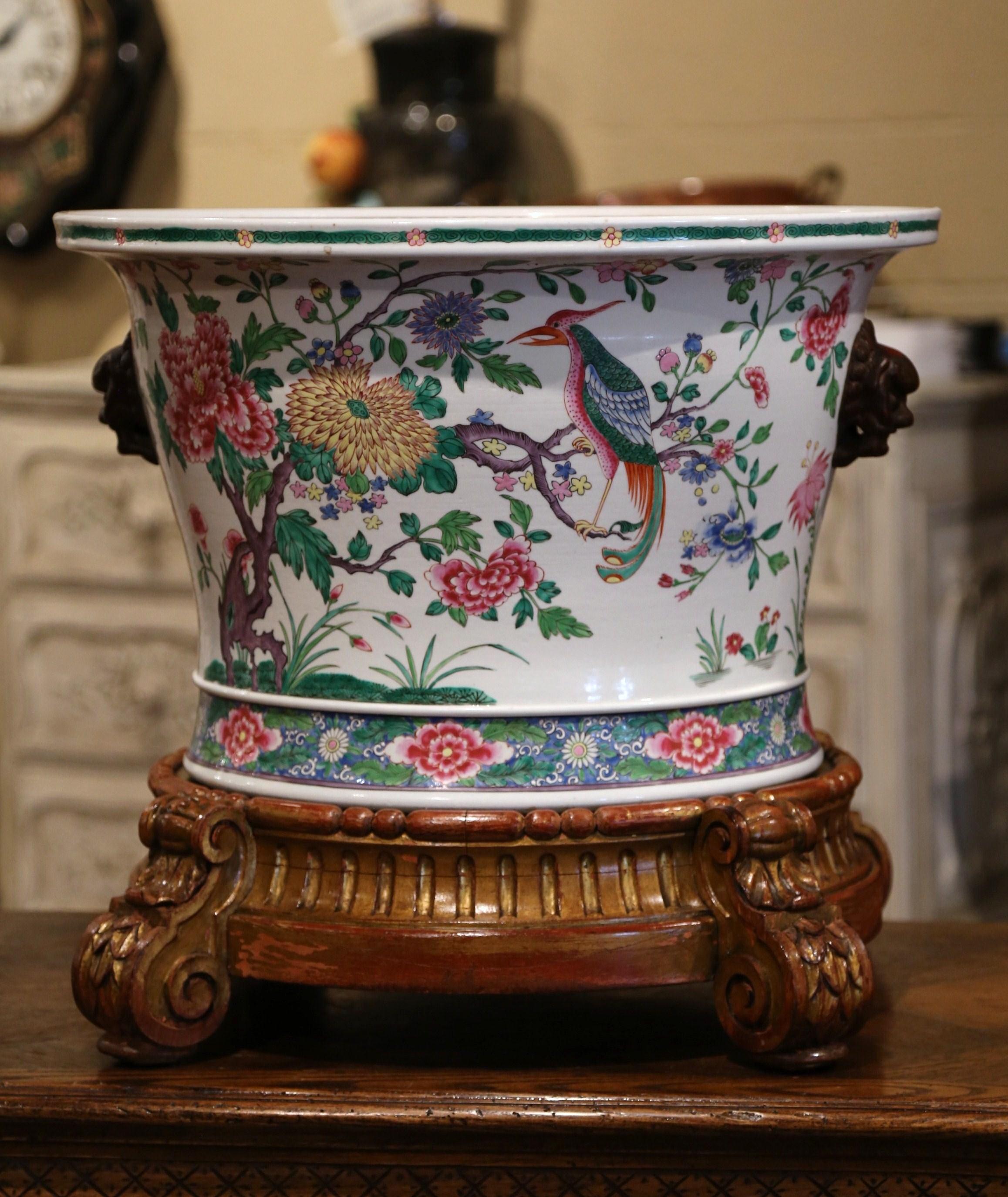 This elegant, colorful antique fishbowl was created in China, circa 1860. Round in shape with figural side handles, the large porcelain cache pot stands on the original carved giltwood base with scroll feet; the bowl features Classical Asian floral