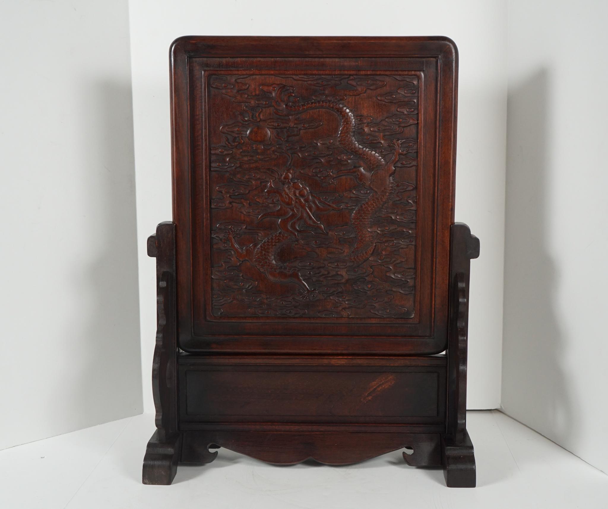 This nice large carved rosewood table screen was created in China, circa 1870. Its carved details depict a dragon flying through celestial clouds in pursuit of a flaming pearl. The workmanship is both intense and subtle with many elements in low