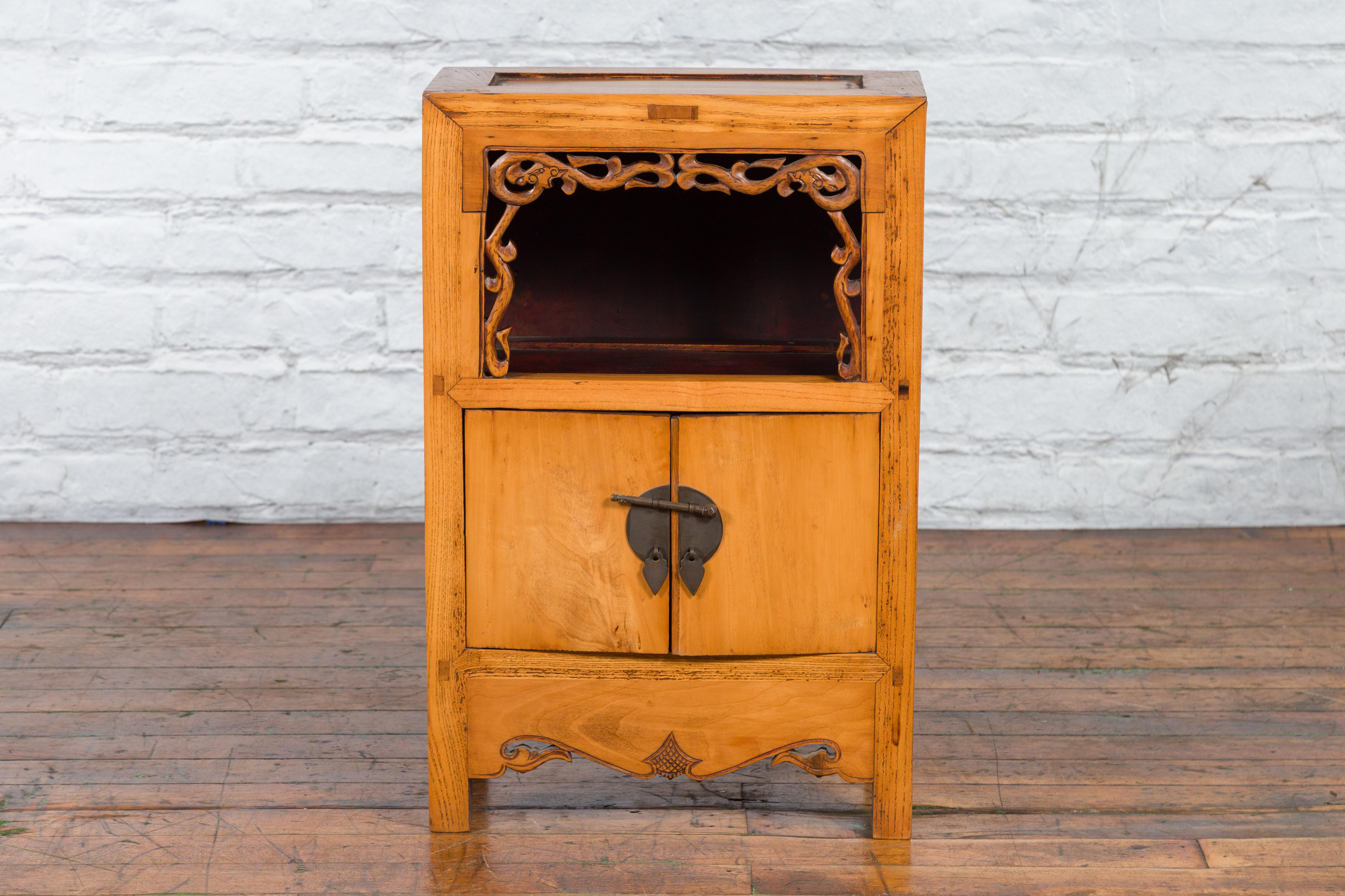A Chinese Qing Dynasty period small cabinet from the 19th century, with carved motifs, open shelf and two doors. Created in China during the 19th century, this small cabinet features a rectangular top with recessed board, sitting above an open shelf