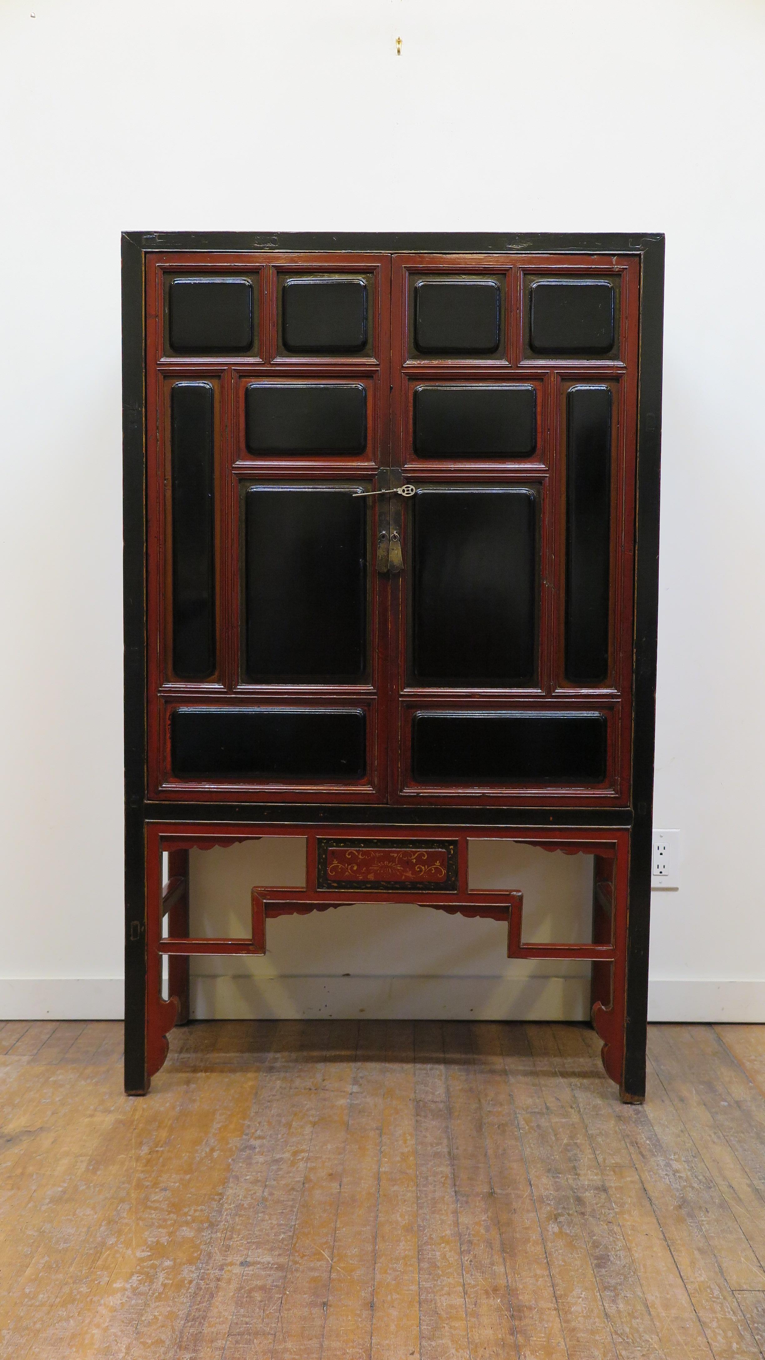 19th century raised panel Chinese cabinet. Very auspicious (favorable) black and red raised panel cabinet. Raised panels decorate the face of the doors. The lower front having geometric apron with scalloped spandrel details and a center panel of red