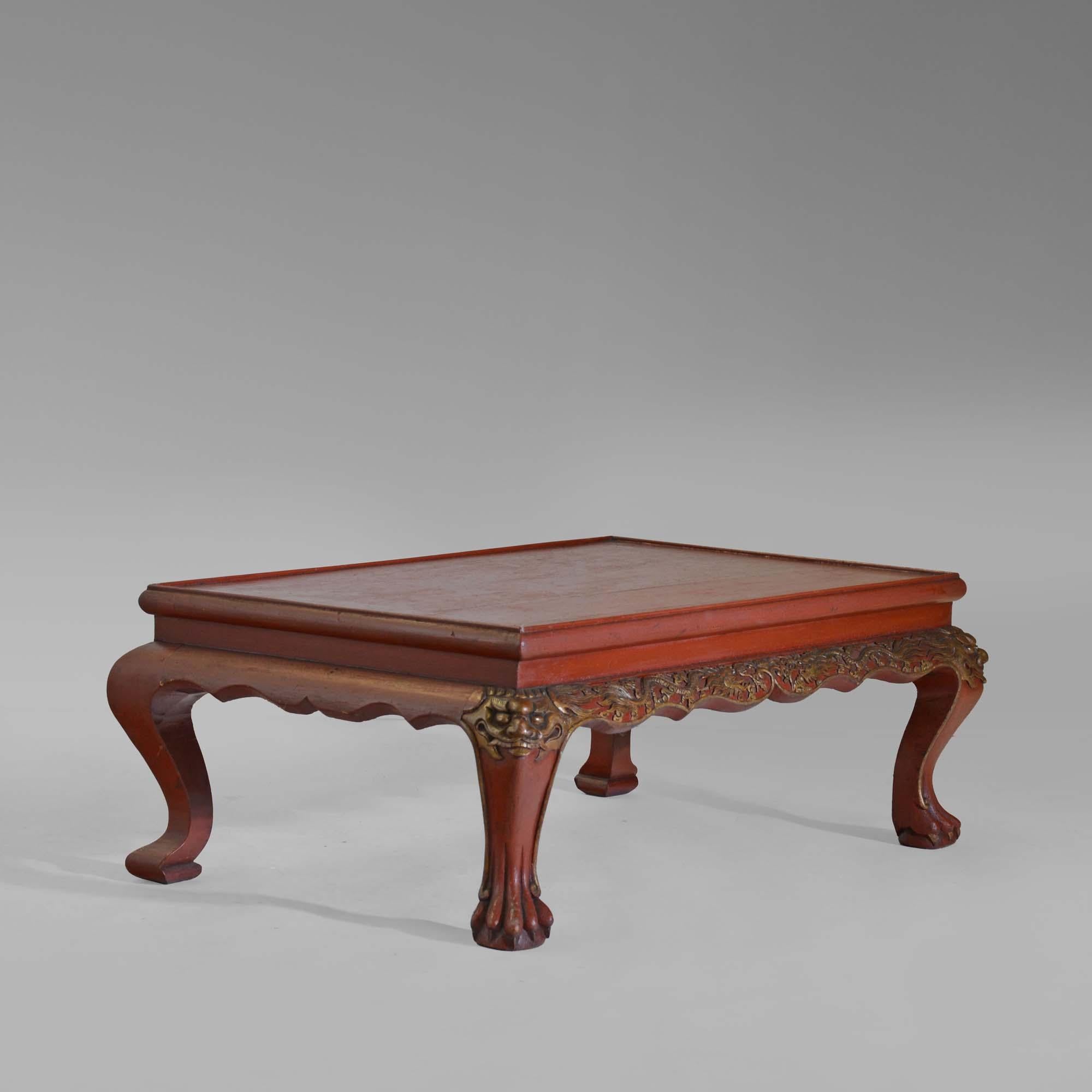 Table basse chinoise en laque rouge du XIXe siècle, composée d'une paire de pieds cabriole à tête de masque sculptés, avec des pieds griffes et boules à l'avant, réunis par une frise sculptée et façonnée avec des sculptures de dragons orientaux