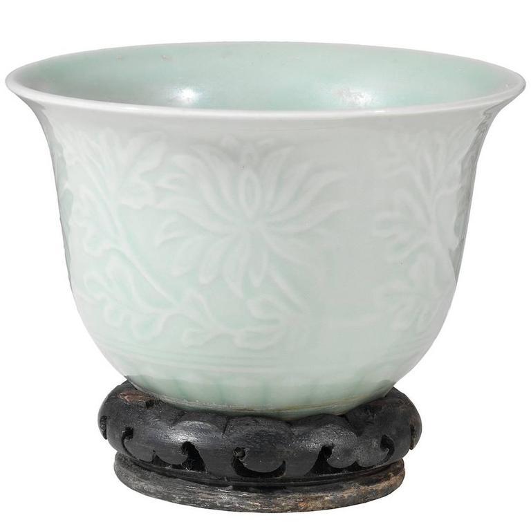 The potted vase is carved with chrysanthemum decoration above a band of upright petals, and is covered inside and out with a glaze of pale-green color. 

Wooden base 

11.4 cm high 