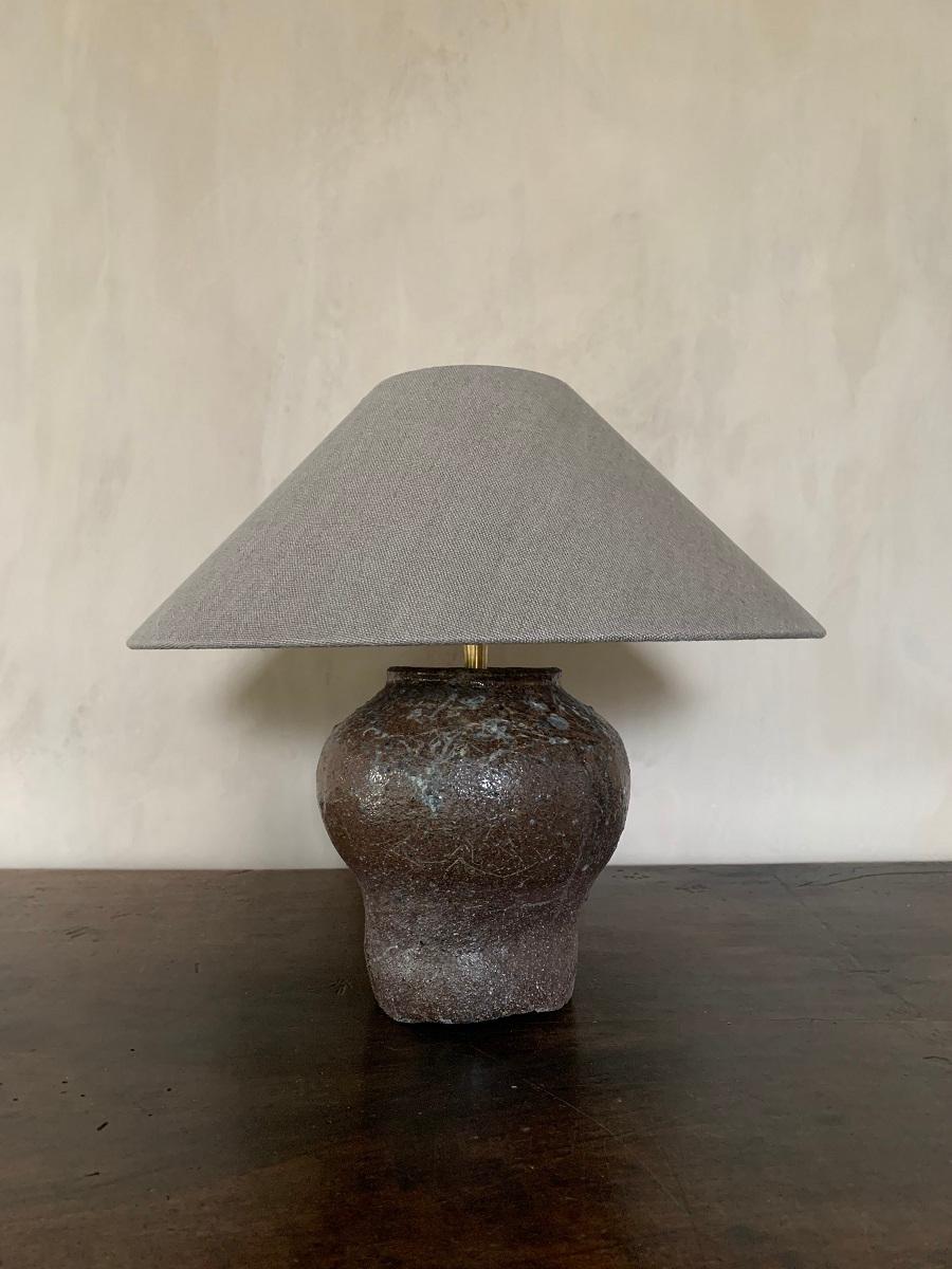 A 19th century rice pot from the Hunan region. The glazed ceramic pot irregularly decorated with an elegant baluster shape. Adapted by our workshop as a table lamp. The hood in Belgian linen.